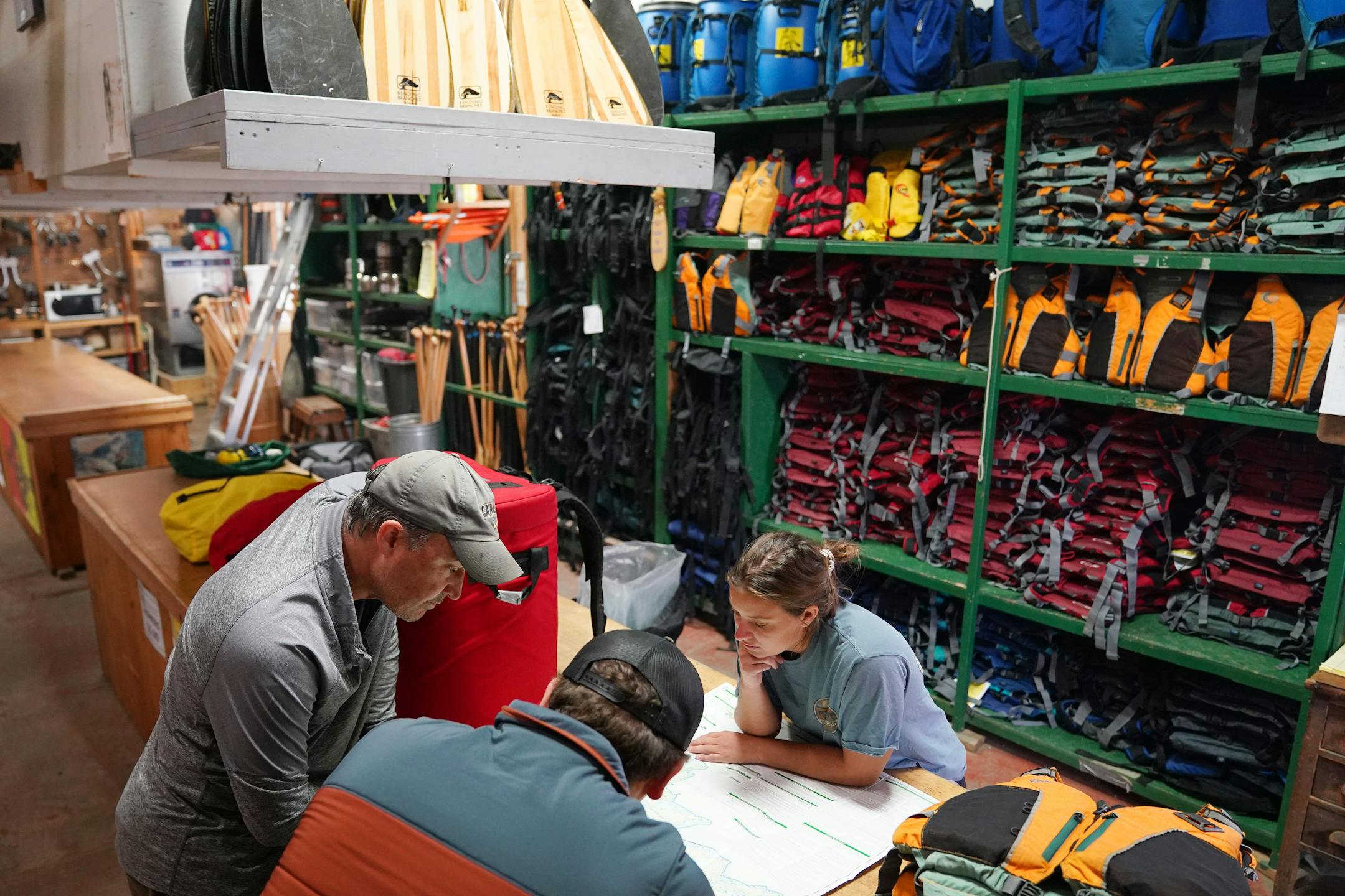Assistant manager Jakob Willschau, bottom, and Emily Roose, right, of Piragis North Woods Co., an outfitter in Ely, showed Adam Battani, left, where to go canoeing Thursday in another part of the Superior National Forest. The Battanis had intended on a five-day trip in the Boundary Waters Canoe Area Wilderness.