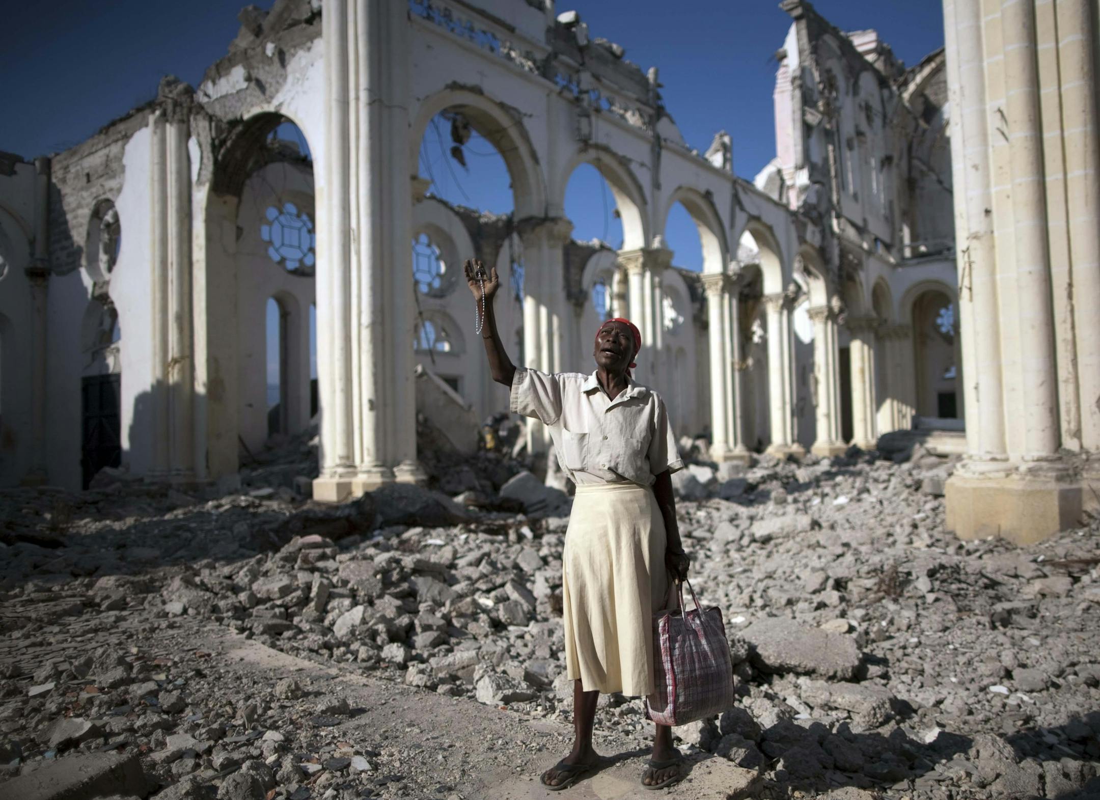 FILE - This combo of two photos shows a Jan. 12, 2010 file photo, top, of Marie La Jesula Joseph praying outside the Cathedral the day it was destroyed by a 7.0 earthquake that struck Port-au-Prince, Haiti, and a photo taken five years later on Jan. 10, 2105, that shows the structure still in disrepair. Recovery has been uneven at best, plagued by poor planning and accusations of graft. (AP Photo/Rodrigo Abd, Dieu Nalio Chery, File)