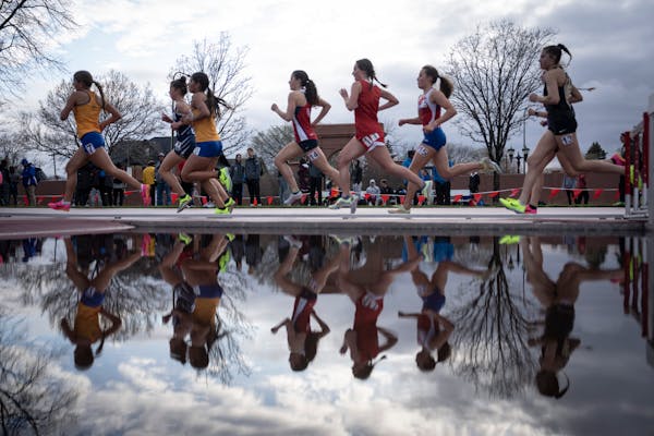 Girls in the 1600 meter dash run past a pool of rain water during the Hamline Elite Meet at Hamline University in St. Paul on Friday.