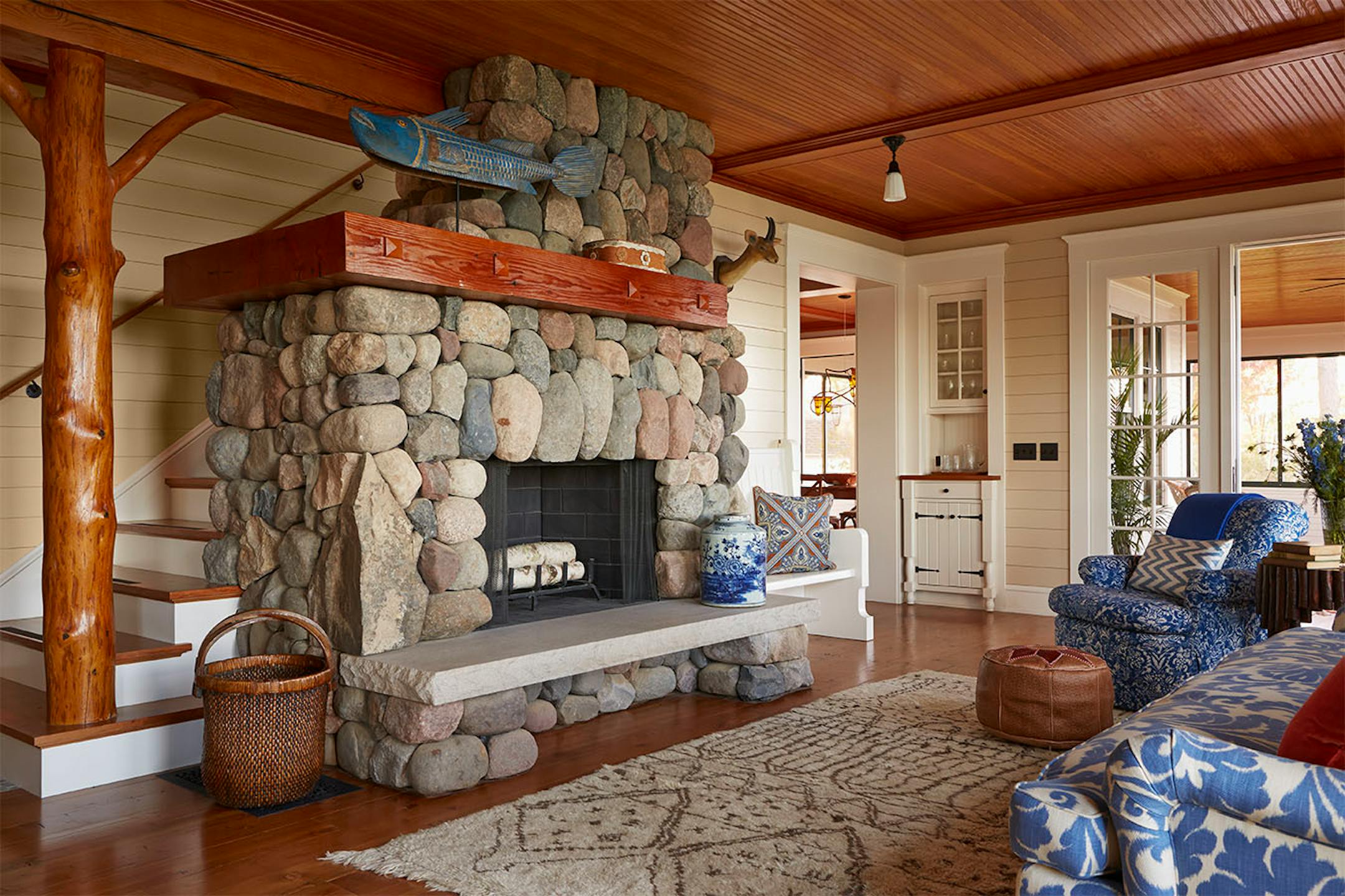 The living room's solid stone wood-burning fireplace is reminiscent of a fishing lodge. Reclaimed trees add rustic character to the staircase.