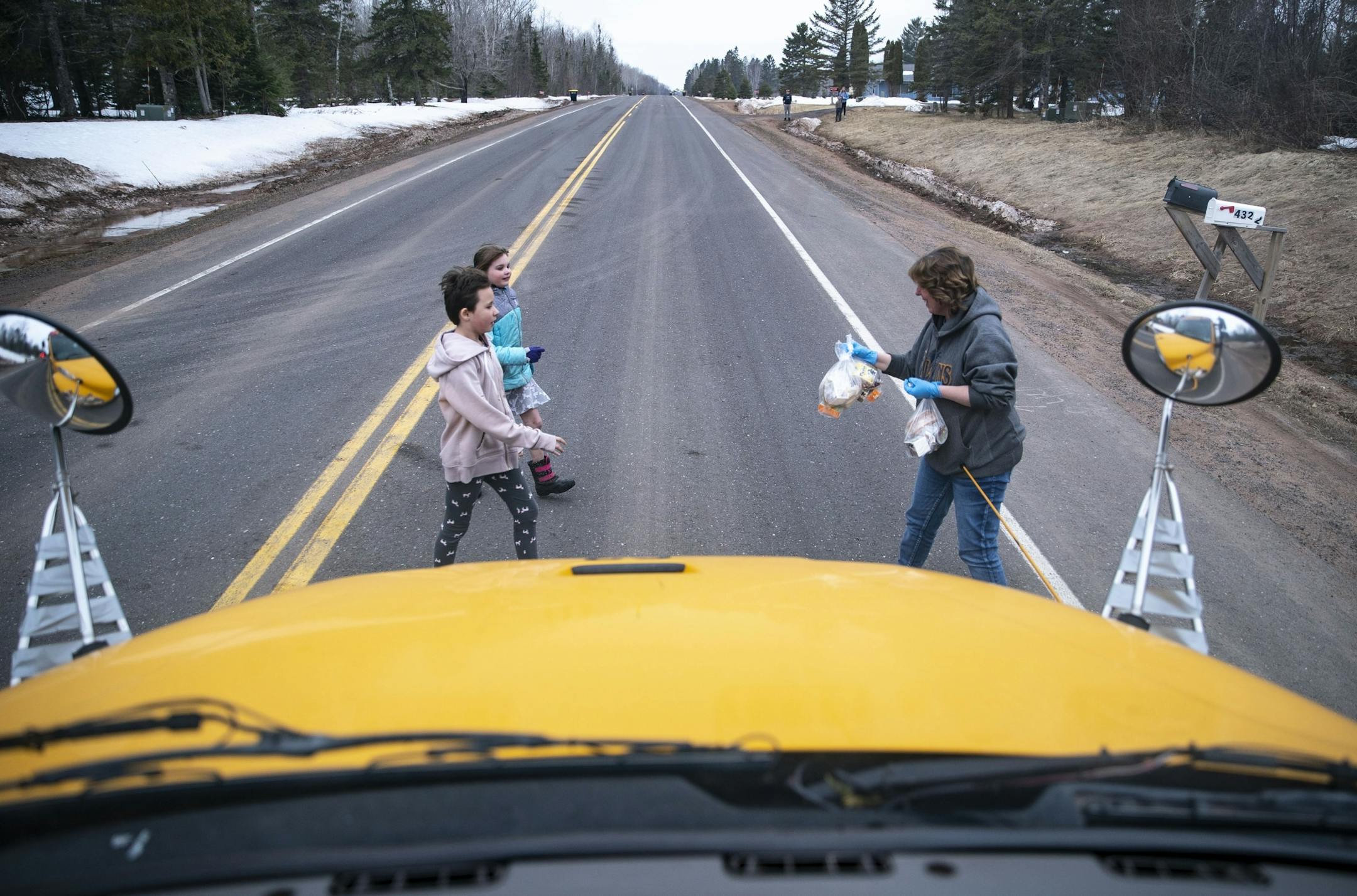 (From left) Aerial and Ryssa Raschke walked across the road to grab their free lunches from Four Corners Elementary School bus driver Michelle Koenen on Wednesday morning.