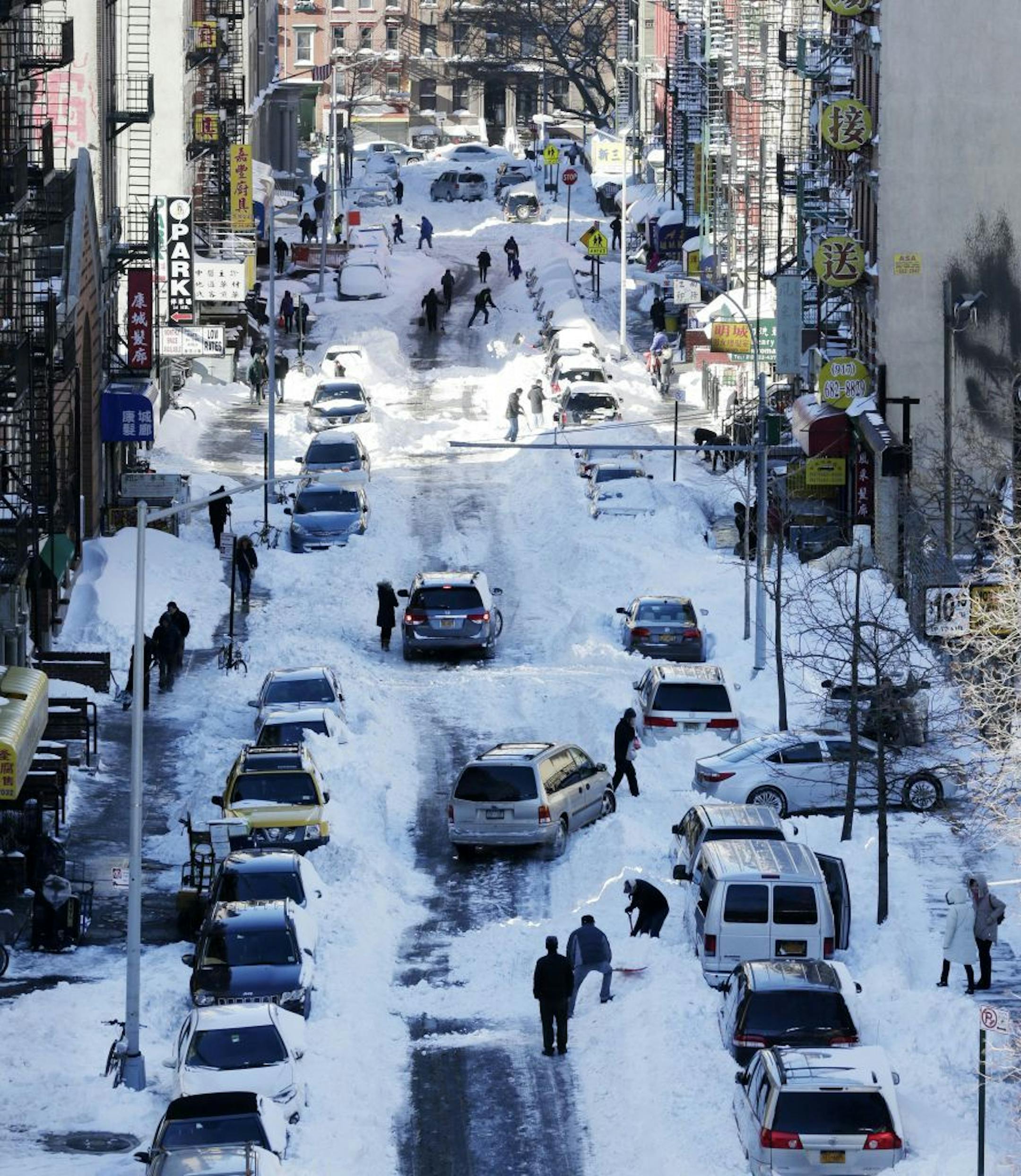 People clear snow from parked cars on Henry Street in the Chinatown neighborhood in New York on Sunday, Jan. 24, 2016. Millions of Americans began digging out Sunday from a mammoth blizzard that set a new single-day snowfall record in Washington and New York City.