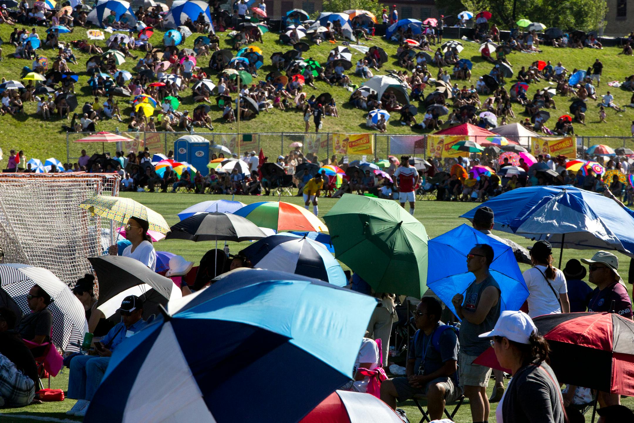 People hold umbrellas to block the sun while watching a soccer game in 2017 at the Hmong Freedom Celebration Festival in St. Paul.