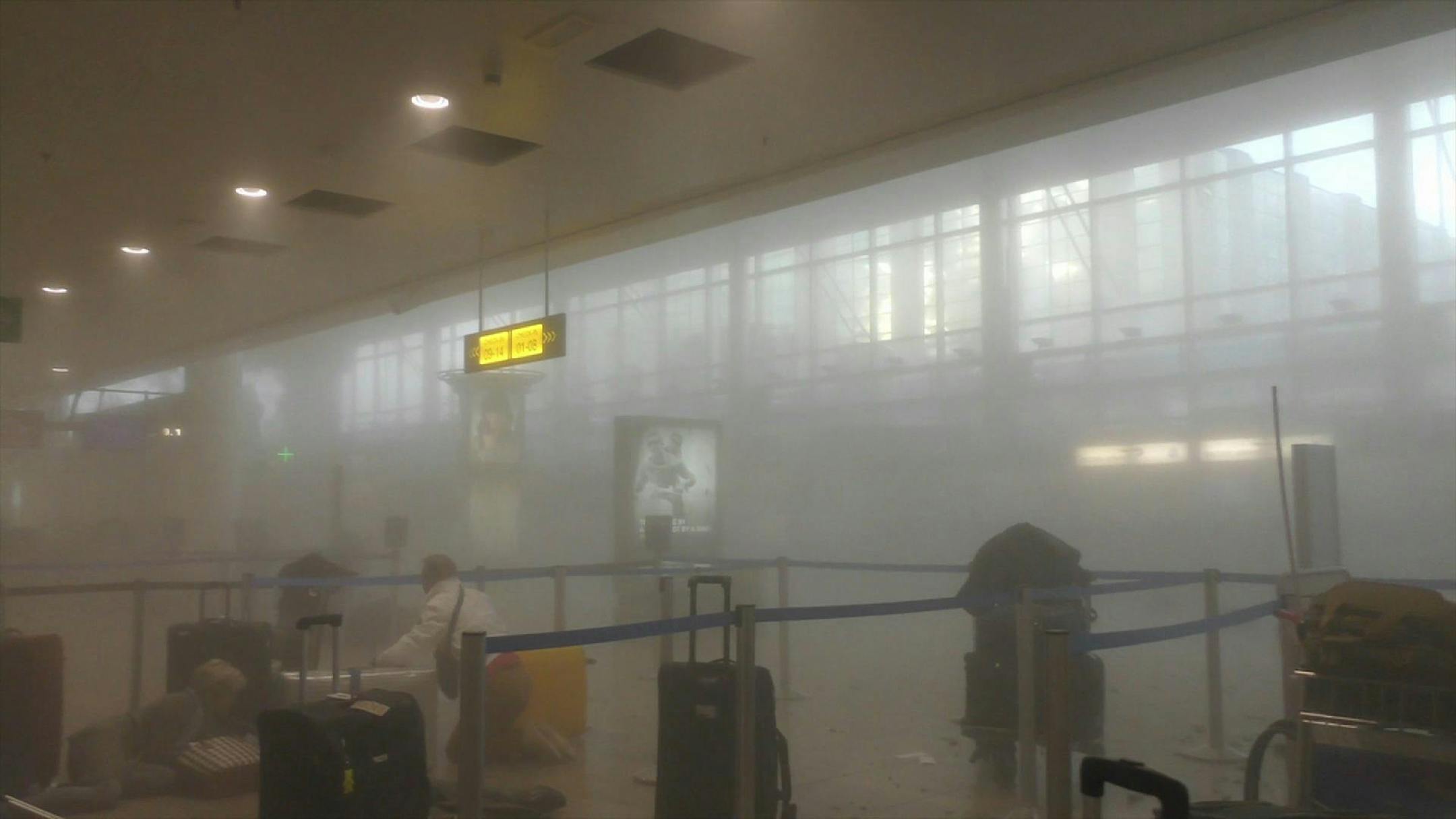 In this photo provided by Ralph Usbeck an unidentified traveller gets to his feet in a smoke filled terminal at Brussels Airport, in Brussels after explosions Tuesday, March 22, 2016. Authorities locked down the Belgian capital on Tuesday after explosions rocked the Brussels airport and subway system, killing a number of people and injuring many more. Belgium raised its terror alert to its highest level, diverting arriving planes and trains and ordering people to stay where they were. Airports a