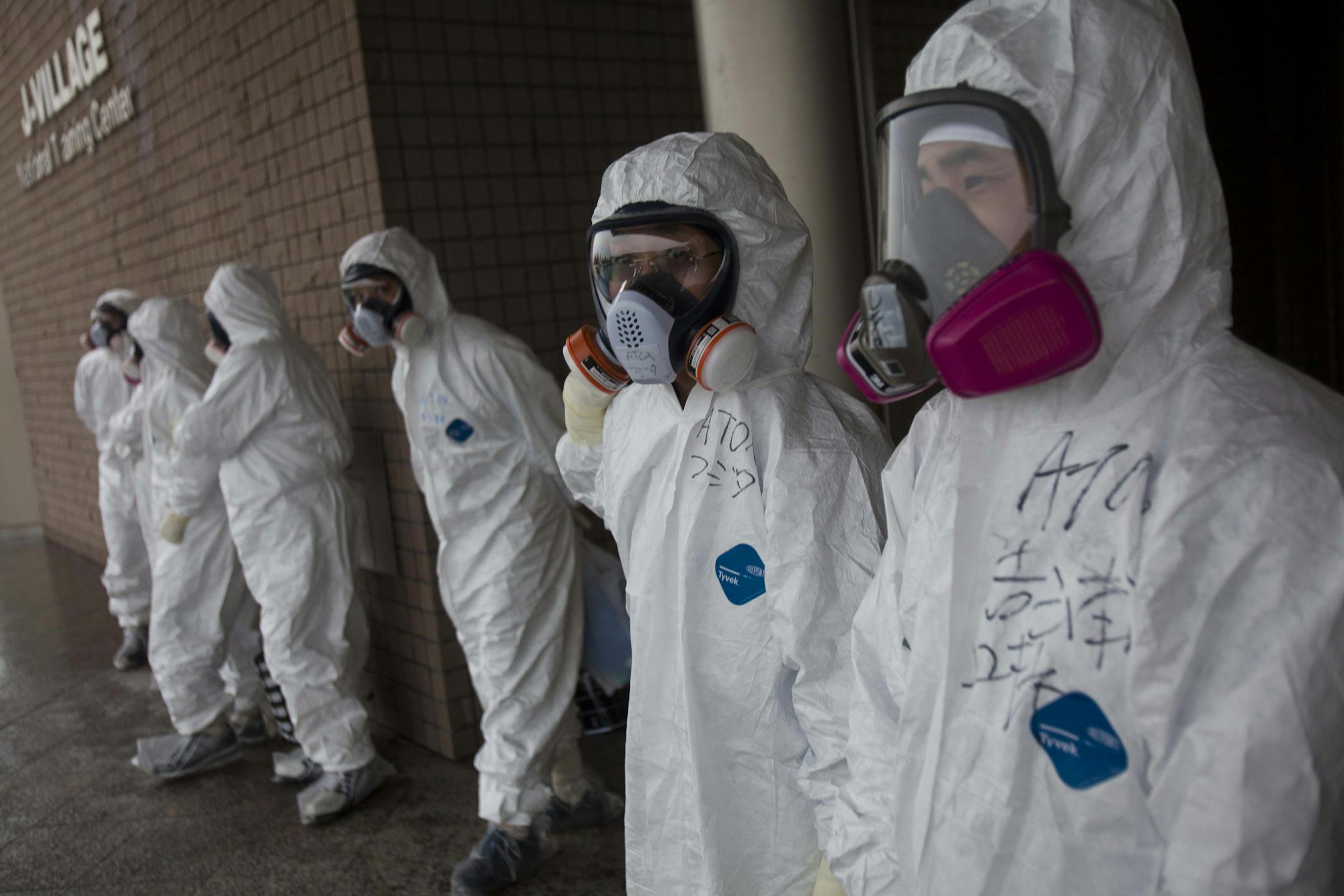 Workers dressed in protective suits and masks wait outside a building at J-Village, a soccer training complex now serving as an operation base for those battling Japan's nuclear disaster at the tsunami-damaged Fukushima Dai-ichi nuclear plant, in Fukushima prefecture, Japan, Friday, Nov. 11, 2011.