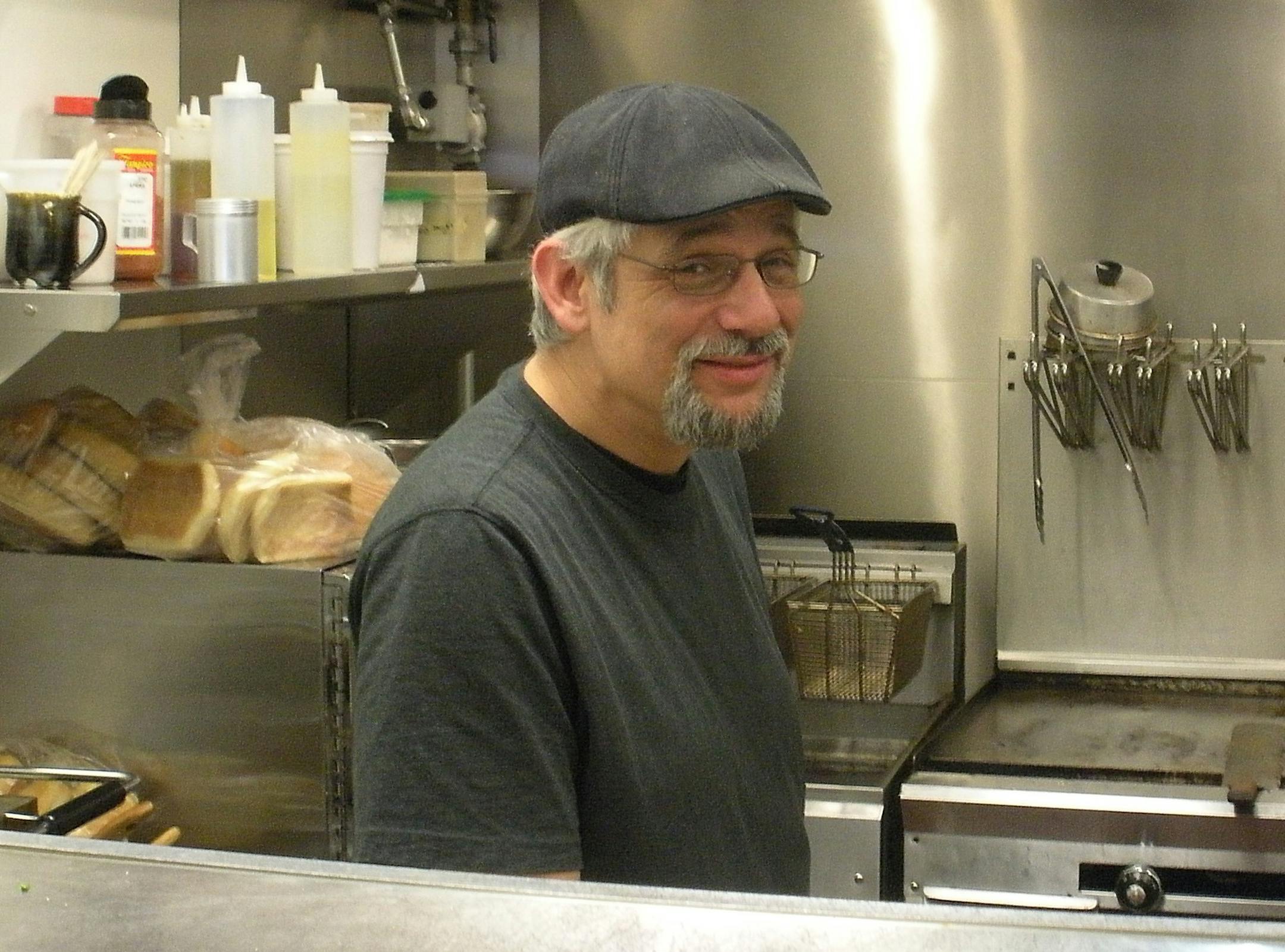 Photo by Jerry Goodrich Artisan Coffee Bistro co-owner with his wife Nan, Ben Peters is rarely, if ever, seen without wearing his cap and a smile.