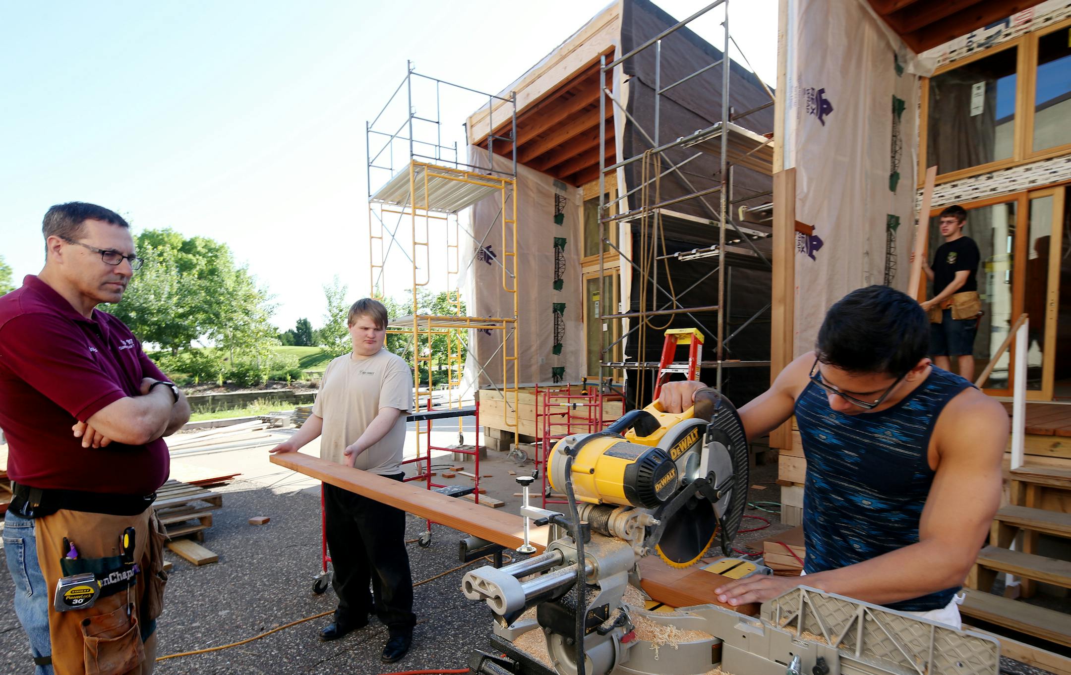 Left to right: Construction Trades Instructor, Paul Landwehr looks over the work of Chad Stubbs (light t-shirt holding board) as Santana Perdomo (dark shirt) cuts a board for the decking for the new camper cabin for the Whitetail Woods Regional Park at Dakota Technical College. Austin Long (background ) works on the siding of one of the three cabins being built. ] JOELKOYAMA‚Ä¢jkoyama@startribune Rosemount, MN on June 2, 2014. Camper cabins are being made by high school students
