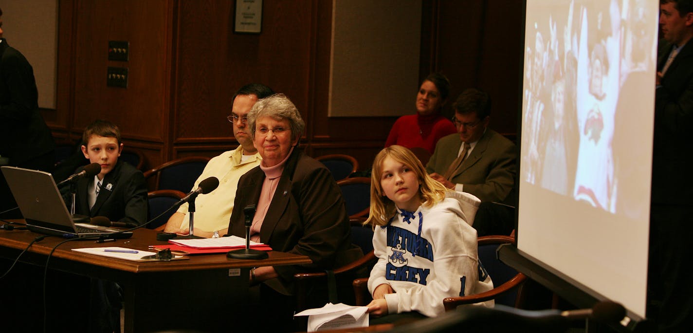 Sen. Gen Olson, R-Minnetrista, flanked by sixth-graders Brendan Broviak, left, and Hannah Ehresmann, watched a video clip about hockey in Minnesota during a committee meeting on Wednesday at the State Capitol. The students are seeking to make hockey the official state sport.