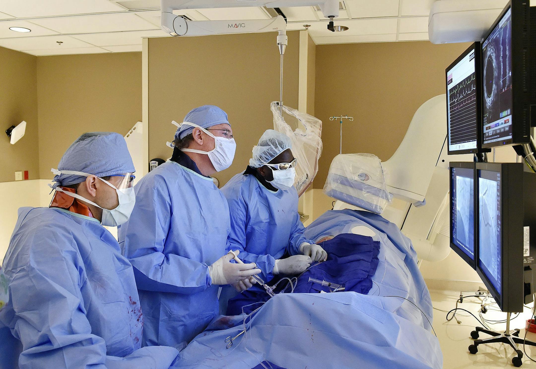Kenneth Huber, middle, an interventional cardiologist with Saint Luke's Mid America Heart Institute, deploys a coronary stent through the femoral artery of a patient with a blocked artery on November 25, 2015. Assisting Huber were cardiology fellow Abdel-Karim Abdul-Rahman, left, and interventional fellow Clarence Findley. (Jill Toyoshiba/Kansas City Star/TNS)