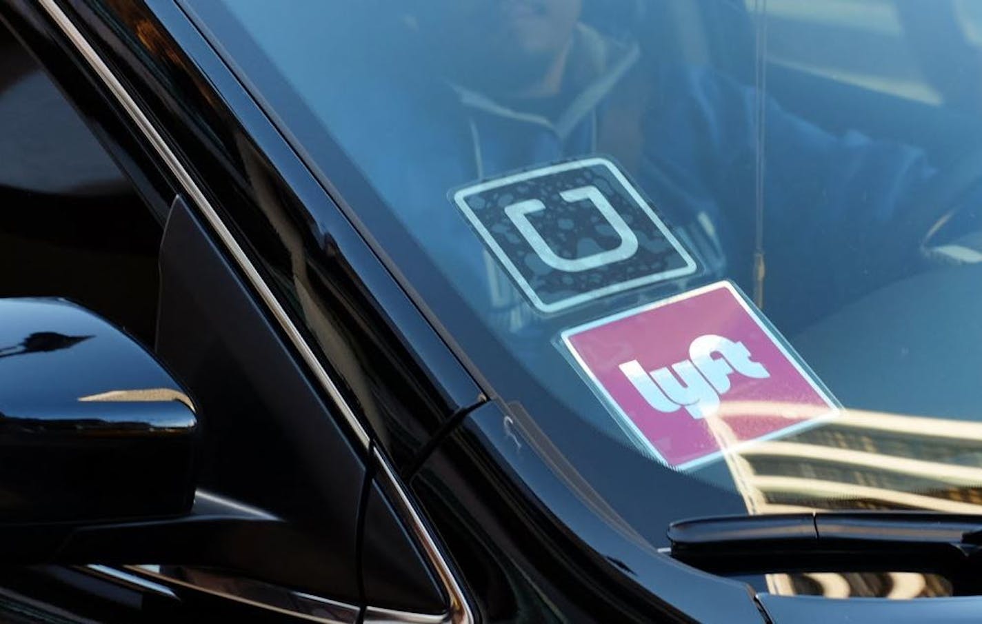 In this Tuesday, Jan. 12, 2016 photo, a driver displaying Lyft and Uber stickers on his front windshield drops off a customer in downtown Los Angeles.