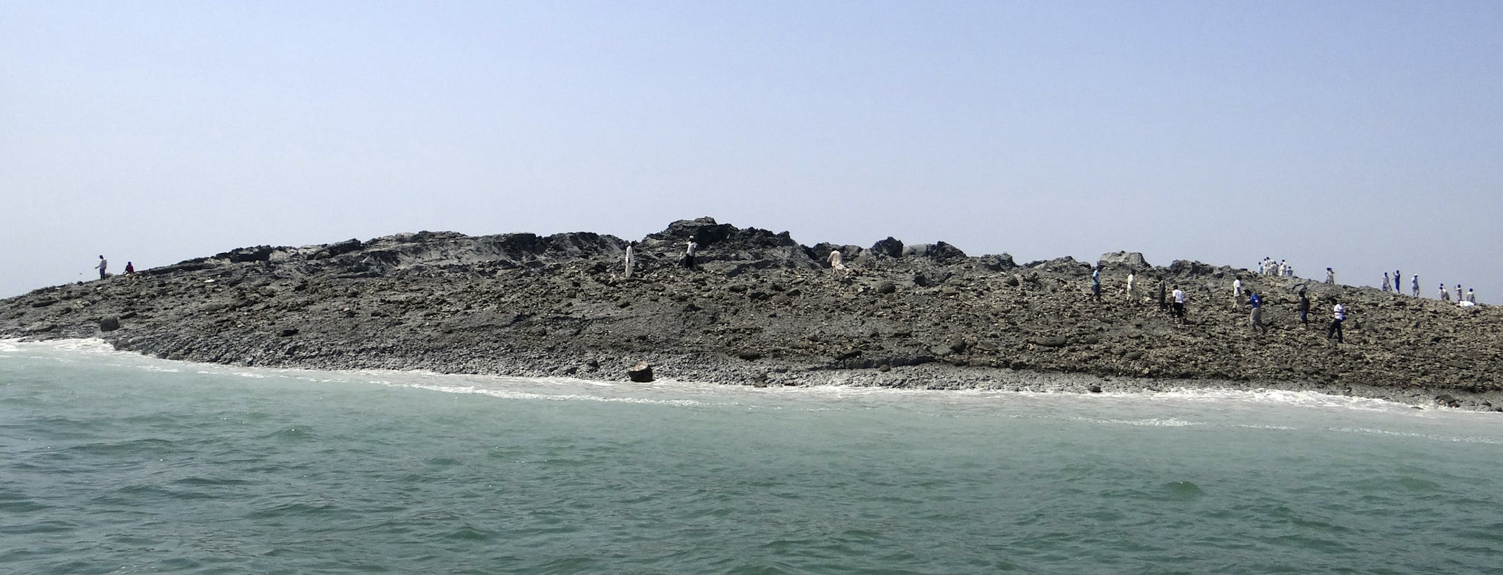 In this photo released by the Gwadar local government office on Wednesday, Sept 25, 2013, people walk on an island that reportedly emerged off the Gwadar coastline in the Arabian Sea. A deadly magnitude 7.7 earthquake struck in the remote district of Awaran in Pakistan's Baluchistan province with enough force to create a small island visible off the southern coast, Pakistani officials said. (AP Photo/Gwadar local government office)