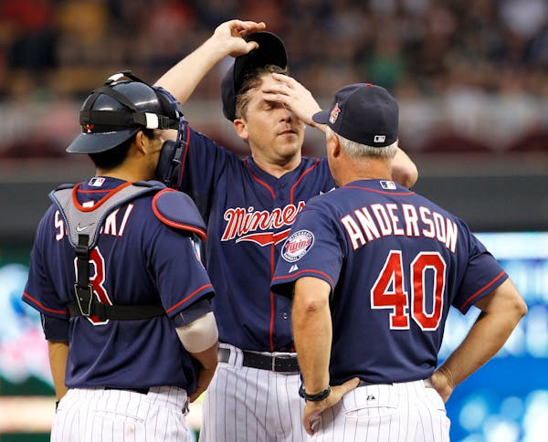 Minnesota Twins starting pitcher Kevin Correia, center, wipes his forehead as he talks with catcher Kurt Suzuki (8) and pitching coach Rick Anderson a
