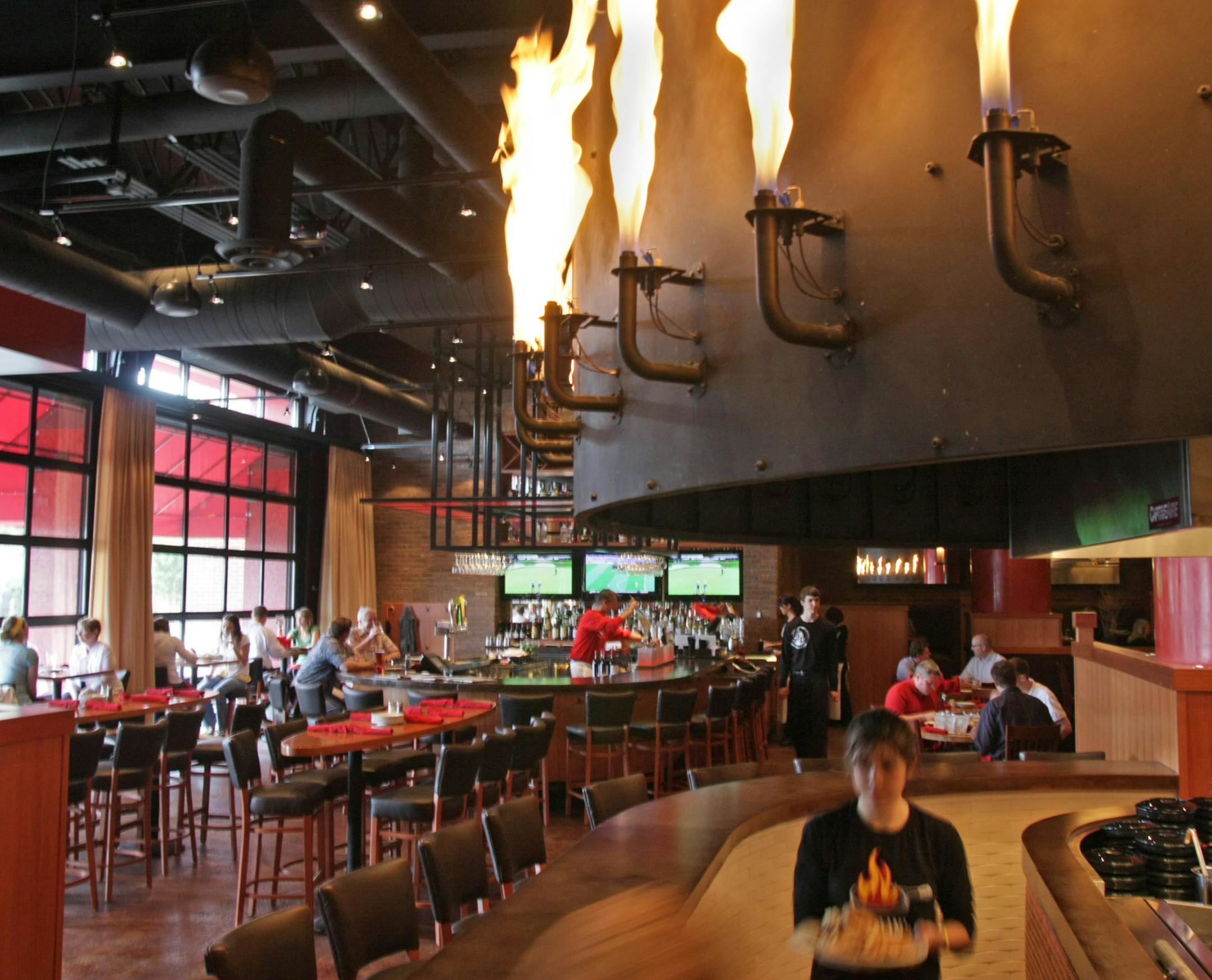 Wait-staff carries food under the large metal canopy with gas jets of flames at the newly-opened Flame in Rosedale.