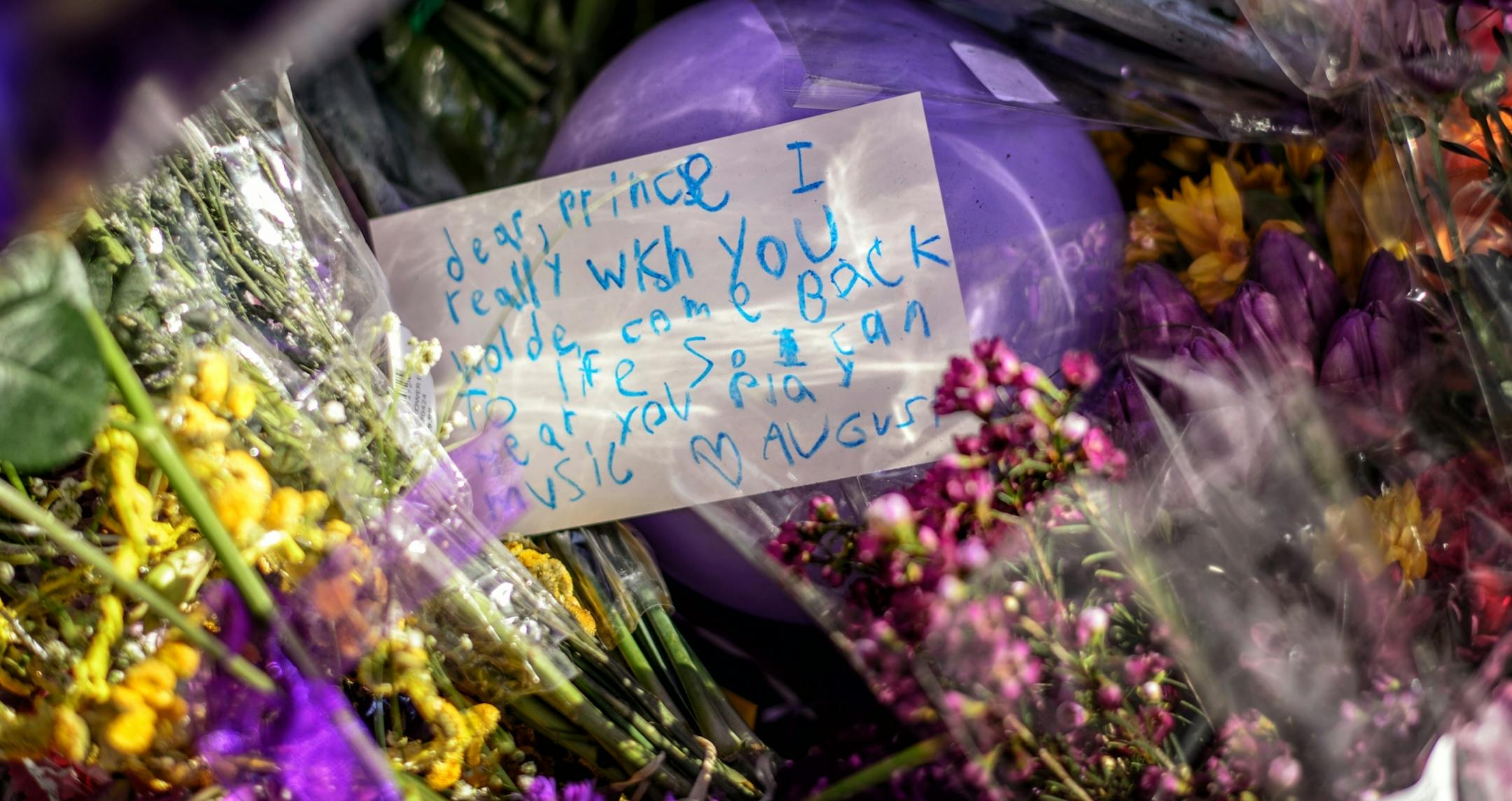 People filed past the makeshift memorial next to Prince's star on First Avenue's wall of stars. They took photos and posed for their own, left letters, purple flowers and balloons. Music by Prince blared from the speakers of passing cars.