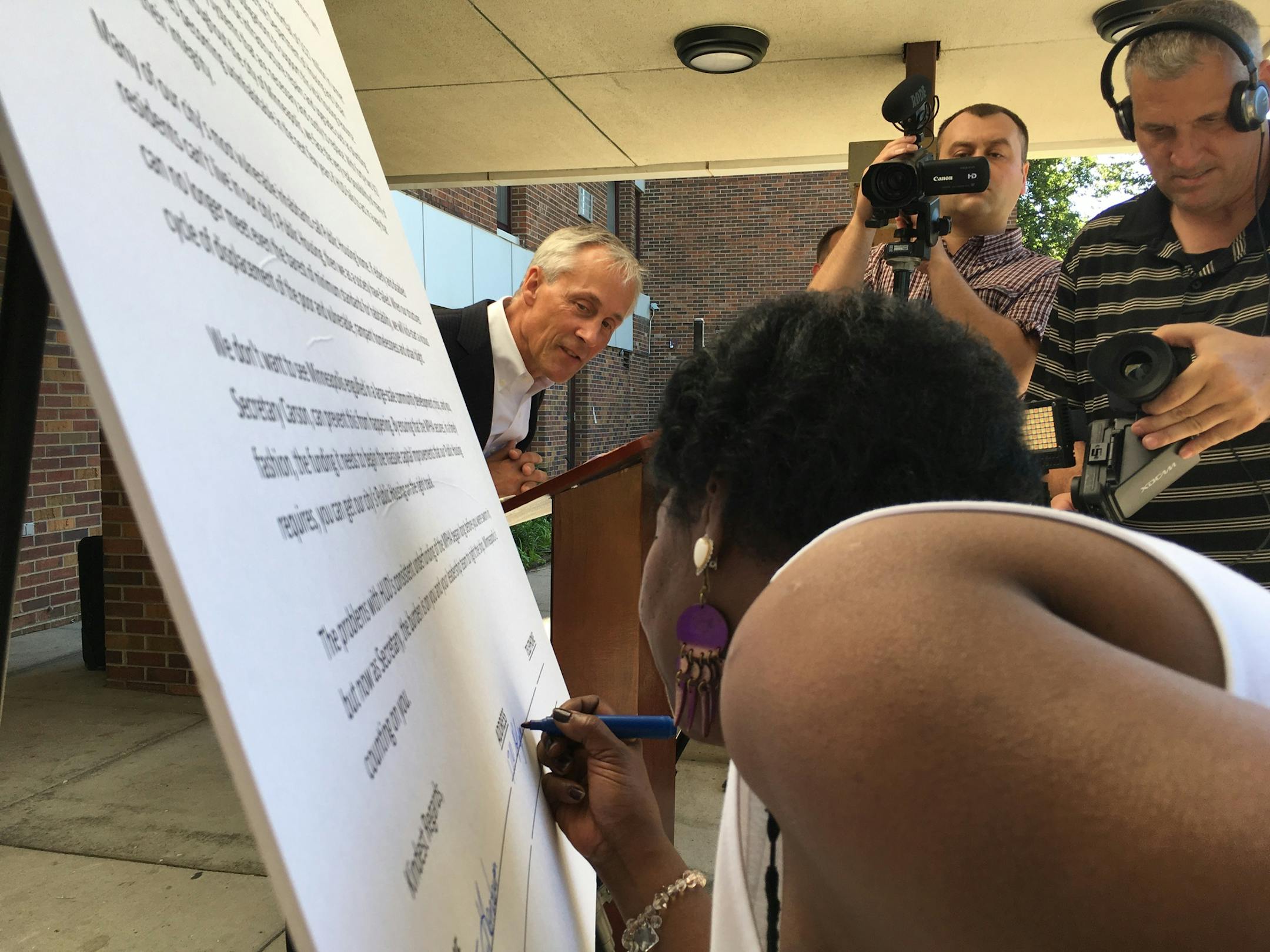 Public housing resident Mattie Henderson signs a letter to HUD Secretary Ben Carson as mayoral candidate Tom Hoch looks on.
