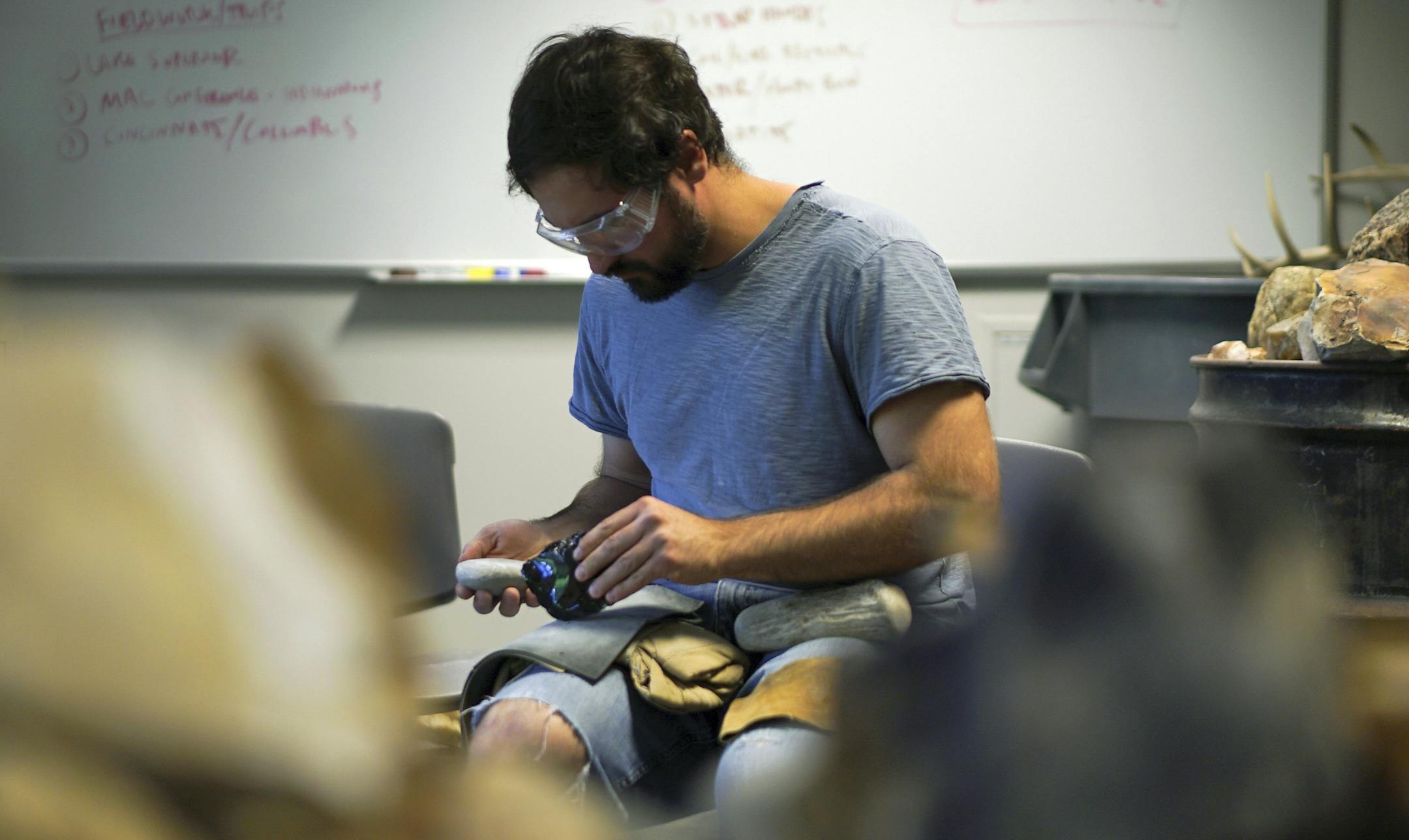 In this June 1, 2017, photo, Metin Eren, an archaeologist at Kent State University, pauses while chipping obsidian in Kent, Ohio. Eren runs a newly-opened laboratory which makes replicas of ancient arrows, knives, and pottery to be shot, crushed, and smashed. It's allowing researchers to learn about engineering techniques of the first native Americans without destroying priceless genuine relics in the process. (AP Photo/Dake Kang)