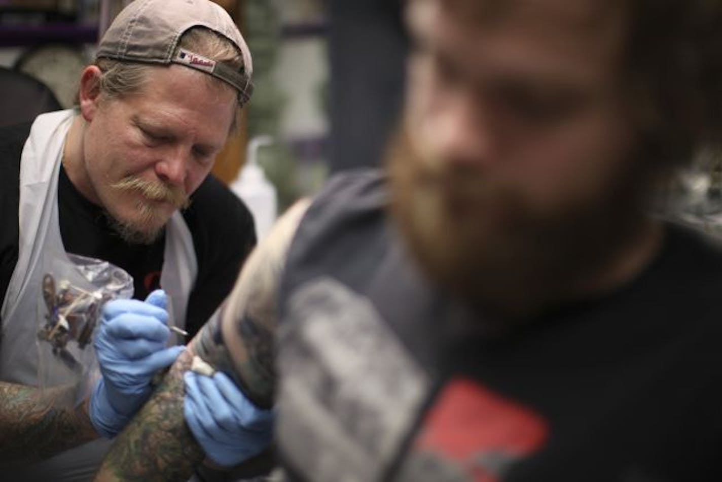 Shahn Anderson inked the artwork on a tattoo he's doing for Jonathan Simmons at his shop, Electric Dragonland, Thursday evening in Hopkins.