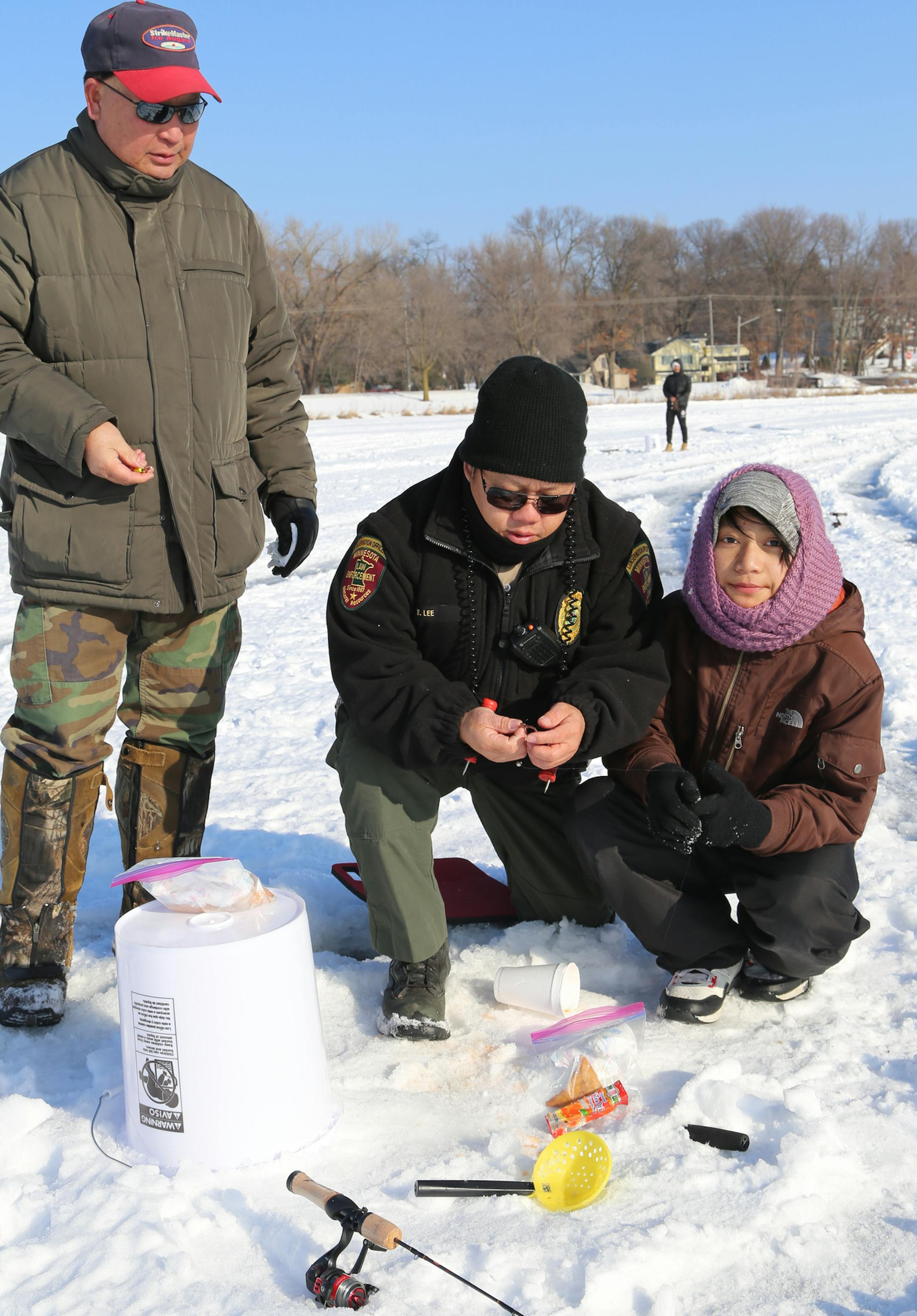 Tong Vang, left, Department of Natural Resources Southeast Asian Community liaison officer, and DNR conservation officer Vang Lee helped a young Karen girl learn about ice fishing on Lake Owasso. The event was sponsored by the Karen Organization of Minnesota.
