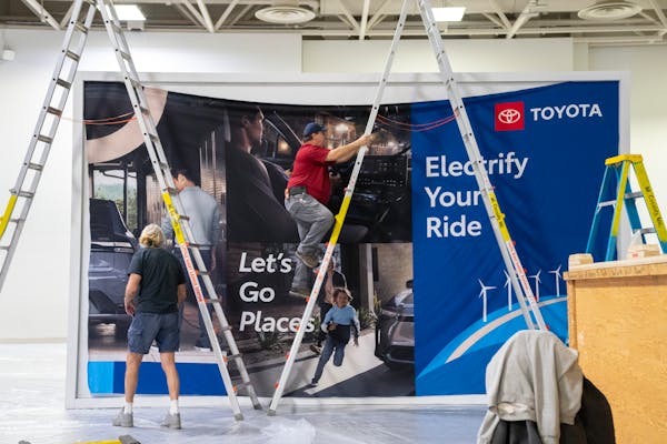 Workers hung up a sign advertising Toyota’s line of electric vehicles during setup for the 2024 Twin Cities Auto Show at the Minneapolis Convention 
