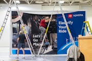 Workers hung up a sign advertising Toyota’s line of electric vehicles during setup for the 2024 Twin Cities Auto Show at the Minneapolis Convention 