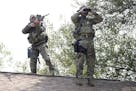 A sniper and a lookout stand on top of a roof searching for two men following the killing of a police officer Tuesday, Sept. 1, 2015 in Fox Lake, Ill.