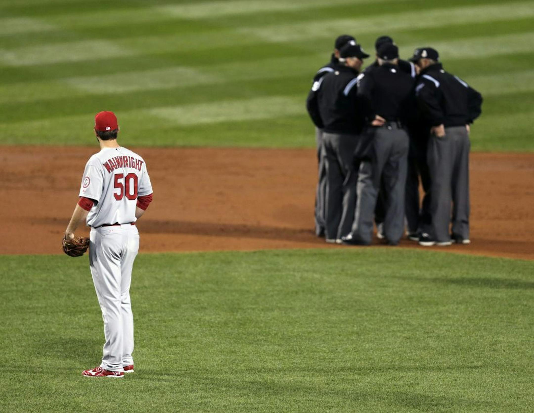 FILE - In this Oct. 23, 2013, file photo, St. Louis Cardinals starting pitcher Adam Wainwright watches as umpires discuss a ruling during the first inning of Game 1 of baseball's World Series against the Boston Red Sox in Boston. Major League Baseball announced Thursday, Jan. 16, 2014, that it will greatly expand instant replay to review close calls starting this season. Each manager will be allowed to challenge at least one call per game. If he's right, he gets another challenge. After the seve