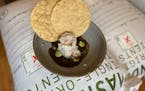 Scallop aguachile like a flower with dabs of salsa verde over a black and lime-scented sauce. Tables are set up next to giant sacks of the heirloom co