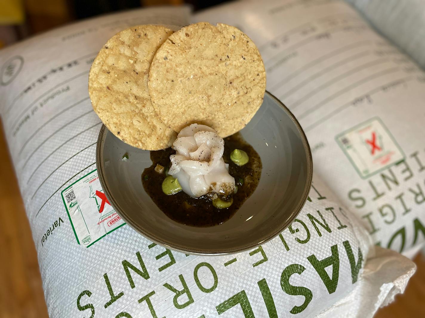 Scallop aguachile like a flower with dabs of salsa verde over a black and lime-scented sauce. Tables are set up next to giant sacks of the heirloom corn that's used in the restaurant's many masa dishes.