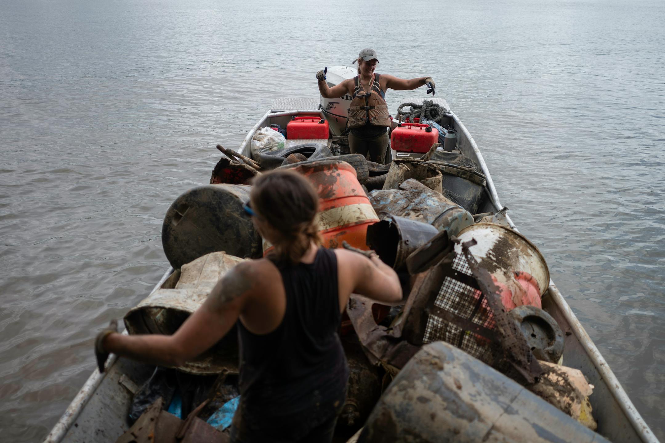 Callie Schaser, background, and Rachel Loomis, foreground, do a dance in their boat after successfully pulling out some trash on Tuesday, July 13, 2021 in Cincinnati, Ohio.