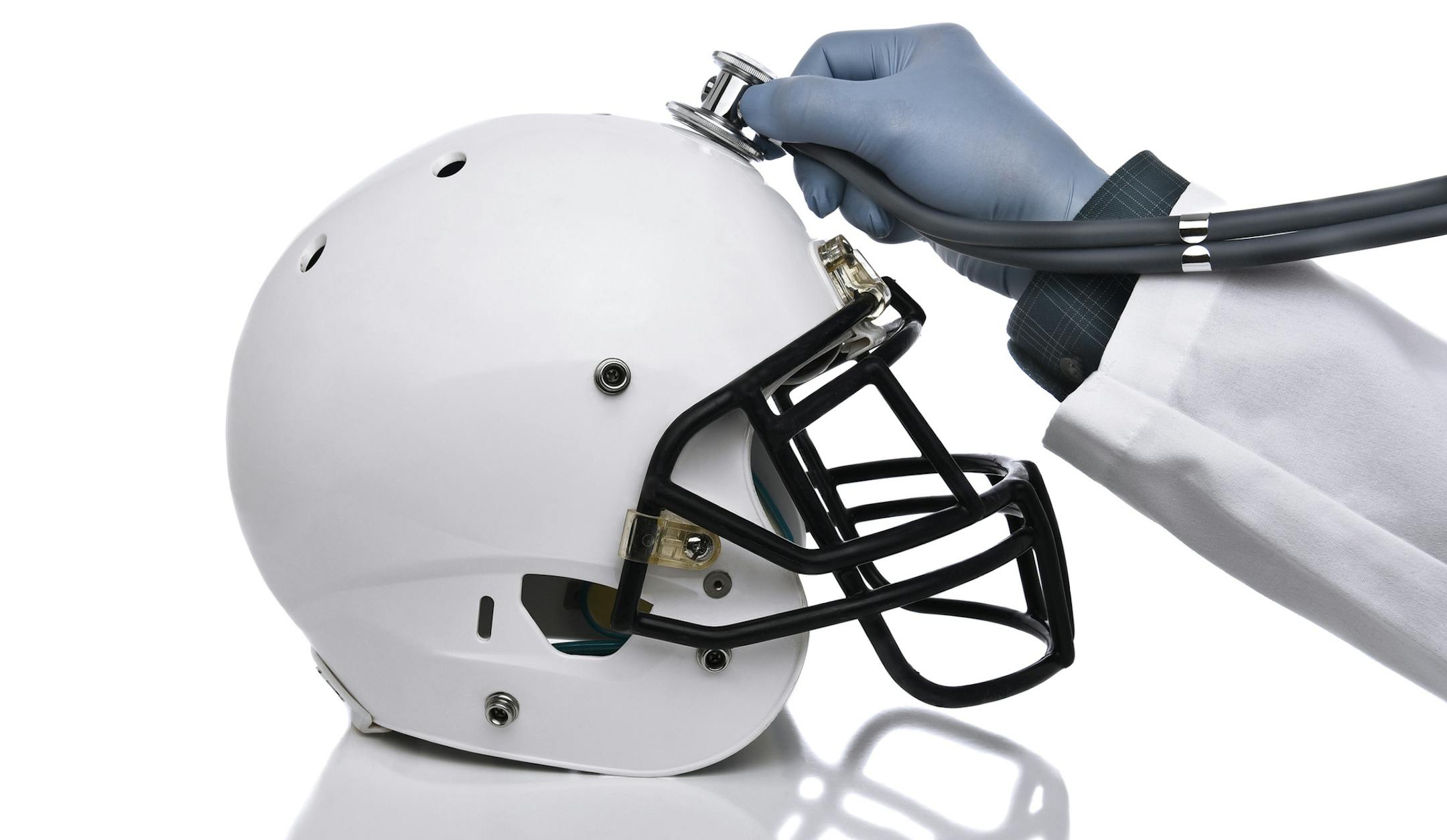 iStock
A football helmet and doctors hand holding a stethoscope on the crown of the helmet. Sports Concussion.