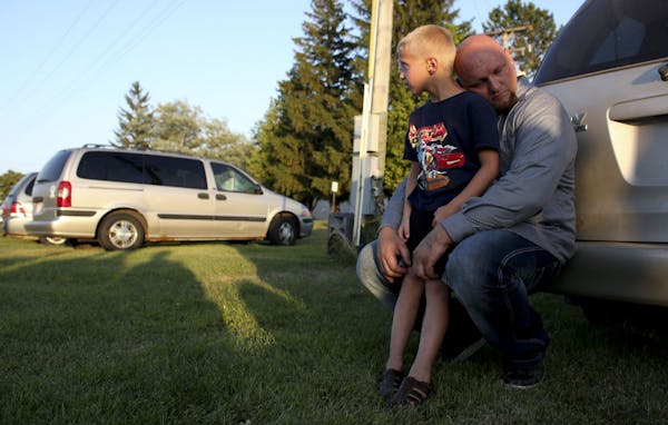 Derrick Koch held his son William, 6, , during a vigil for two year-old Isaiah Theis found dead in a locked car after he went missing in Centuria Wis.