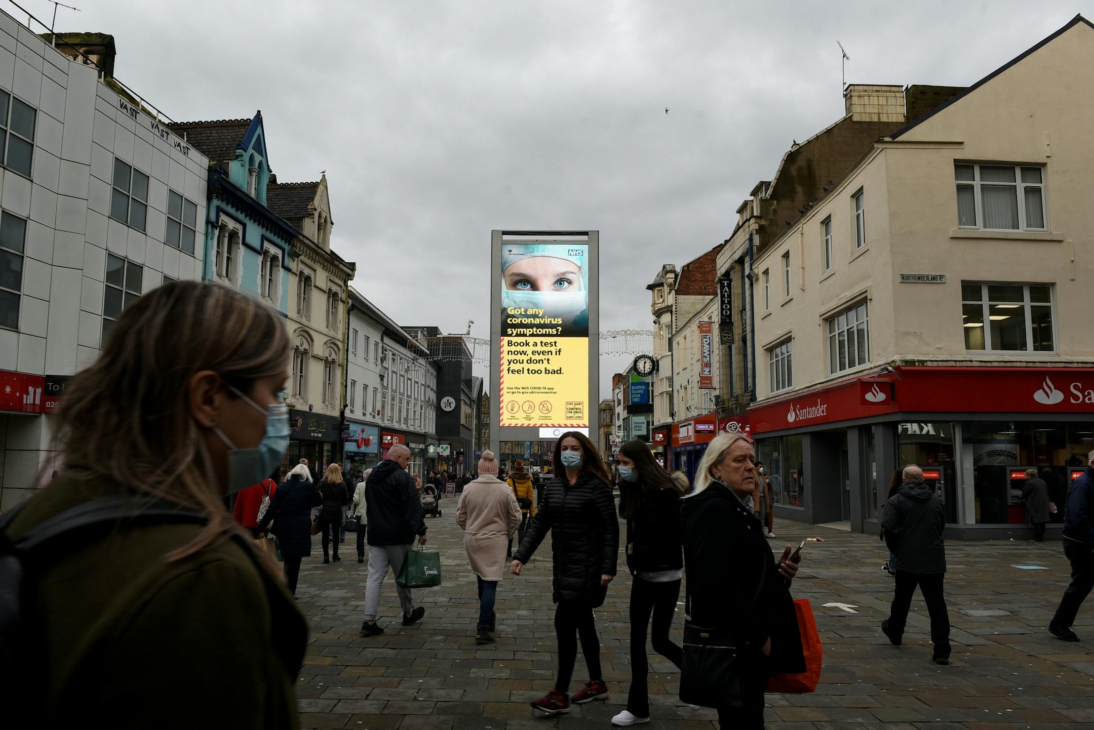 Signs alert shoppers to get tested for the the coronavirus in Newcastle, England, Monday, Dec. 7, 2020, if they are showing signs of the virus. Health officials worry whether enough people will be willing to take a vaccine based on a relatively untested technology.