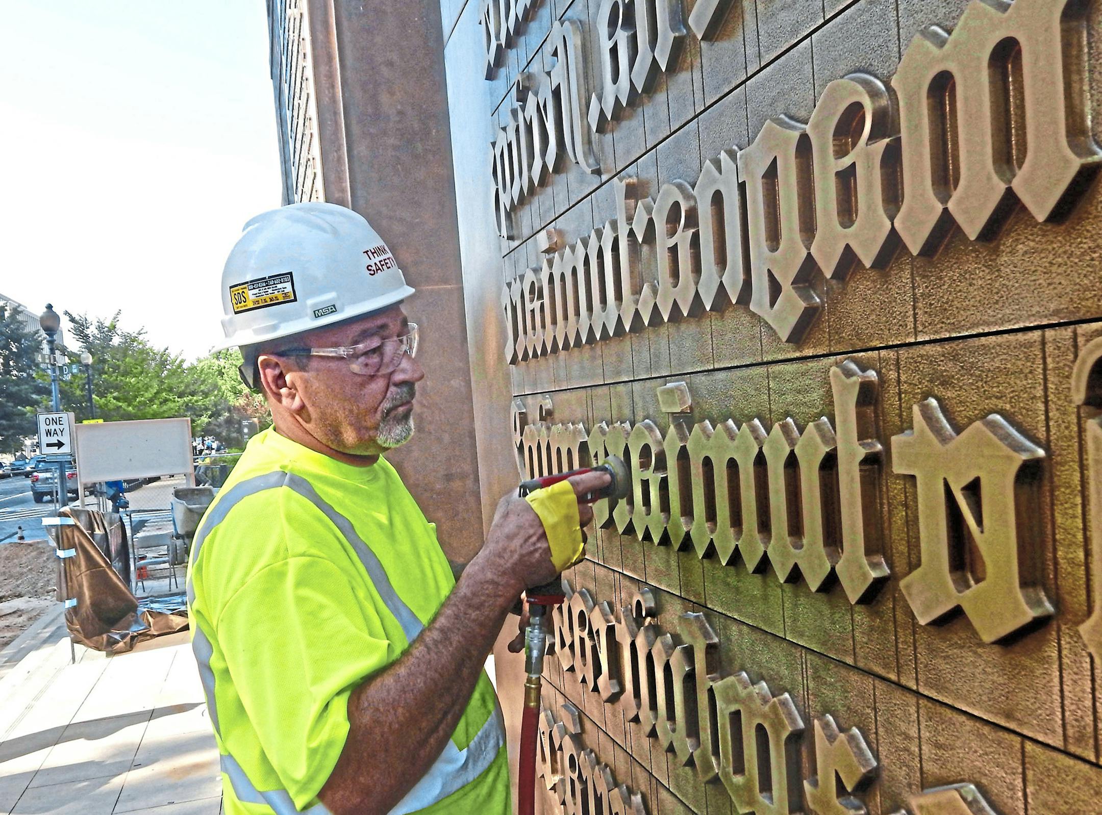 Jack Elliott of the Kansas City foundry Zahner burnishes the 40-foot bronze panels that flank the entrance to the Museum of the Bible in order to age their appearance. Designed by artist Larry Kirkland, the panels are a representation of the first page of Genesis from the Gutenberg Bible. (Tracie Mauriello/Pittsburgh Post-Gazette/TNS)
