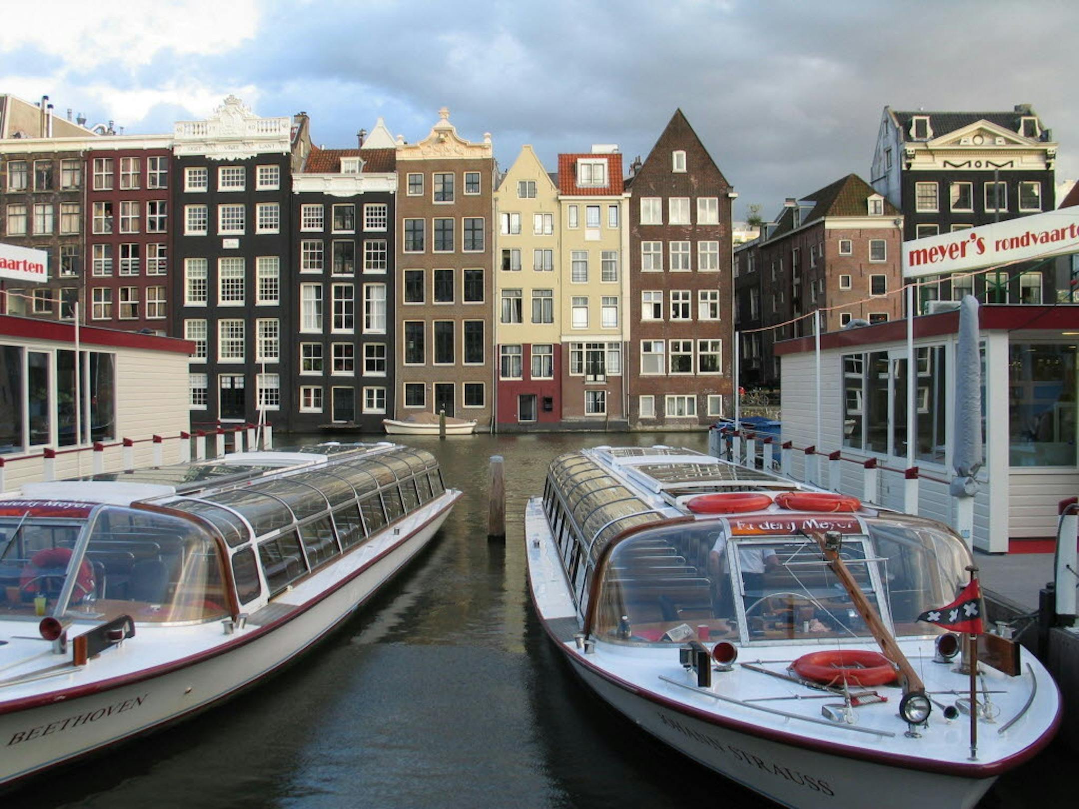 Tour boats await passengers in downtown Amsterdam. Amsterdam's canals criss-cross the old city making it easy to see it by boat. The traditional houses here are tall and skinny, and furniture has to be lifted into the upper rooms from the outside.