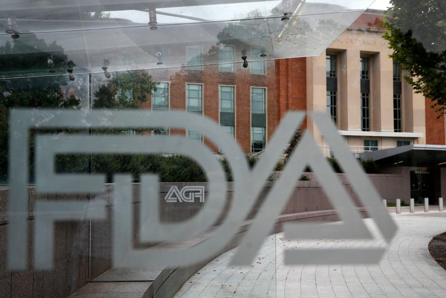 FILE - This Aug. 2, 2018 file photo shows the U.S. Food and Drug Administration building behind FDA logos at a bus stop on the agency's campus in Silver Spring, Md. The Food and Drug Administration has issued a negative review of a closely watched experimental drug for the debilitating illness known as Lou Gehrig's disease. The review comes ahead of a meeting this week for outside experts to vote on the drug for ALS. The drug has been the focal point of a lobbying campaign by patients, their families and lawmakers. FDA reviewers said Monday, March 28, 2022 the single study from Amylyx Pharmaceuticals was "not persuasive" due to missing data, errors in enrolling patients and other problems. (AP Photo/Jacquelyn Martin, File)