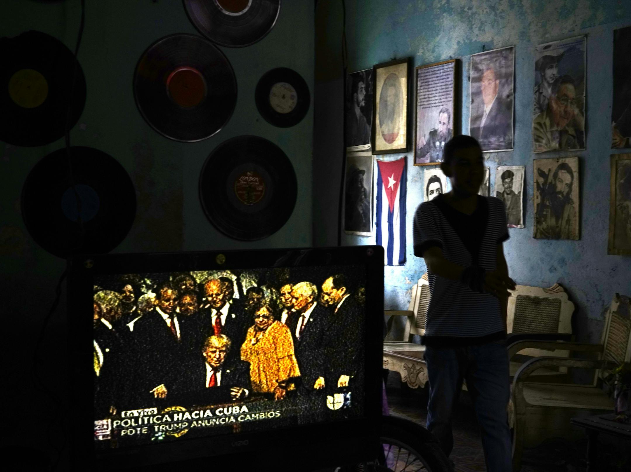 FILE - In this June 16, 2017, file photo, a man walks past a television set showing U.S. President Donald Trump signing the new Cuba policy, in a living room festooned with images of Cuban leaders at a house in Havana, Cuba. President Trump declared he was restoring some travel and economic restrictions on Cuba that were lifted as part of the Obama administration's historic easing. (AP Photo/Ramon Espinosa, File)