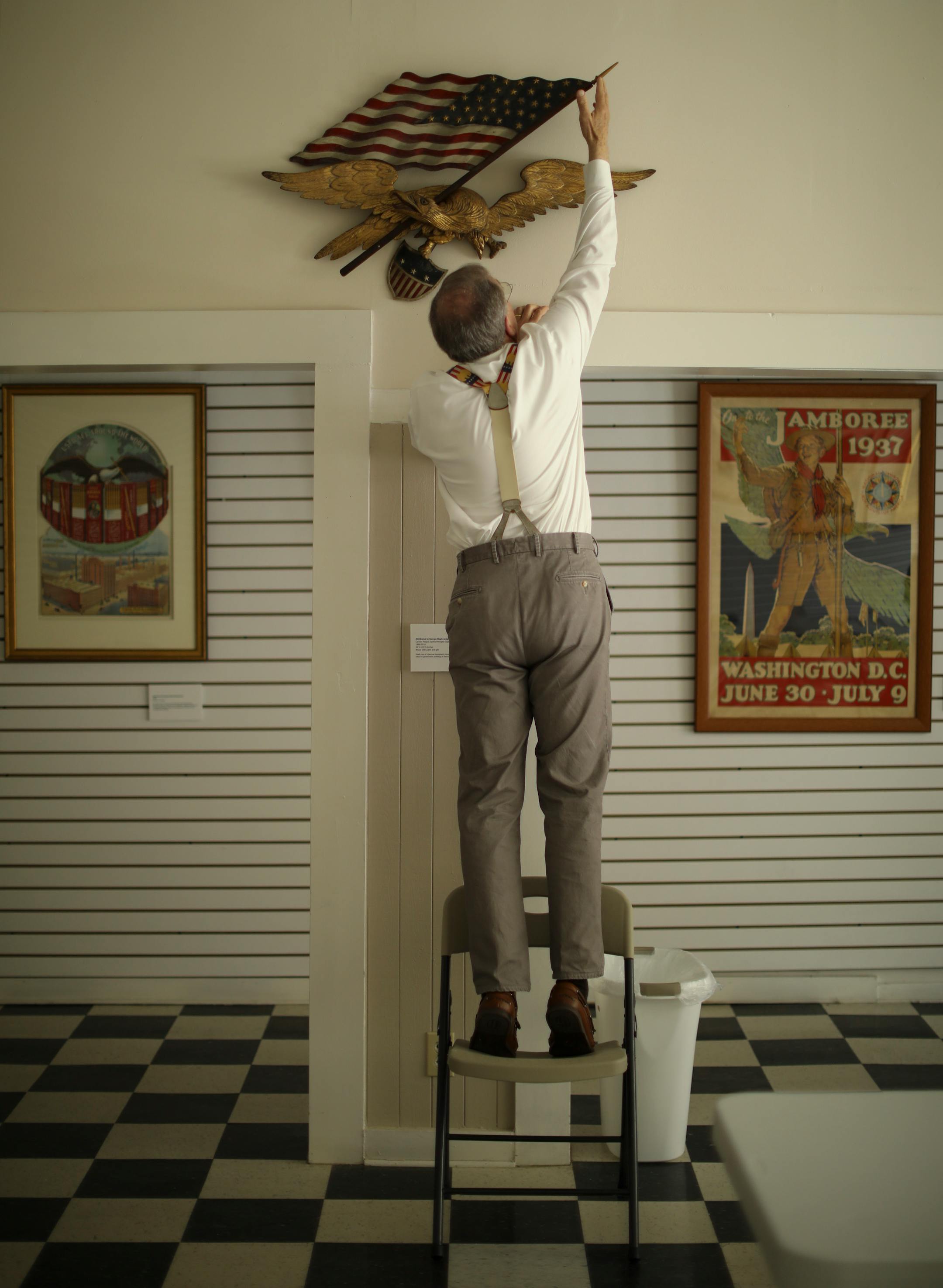 Very much a hands-on collector, Preston Cook stood on a folding chair to adjust the tip of a flagpole on the carved wooden plaque of a spread-winged eagle, with flag and shield, circa 1890-1910 and attributed to George Stapf. The work is among the artworks he donated to the National Eagle Center.