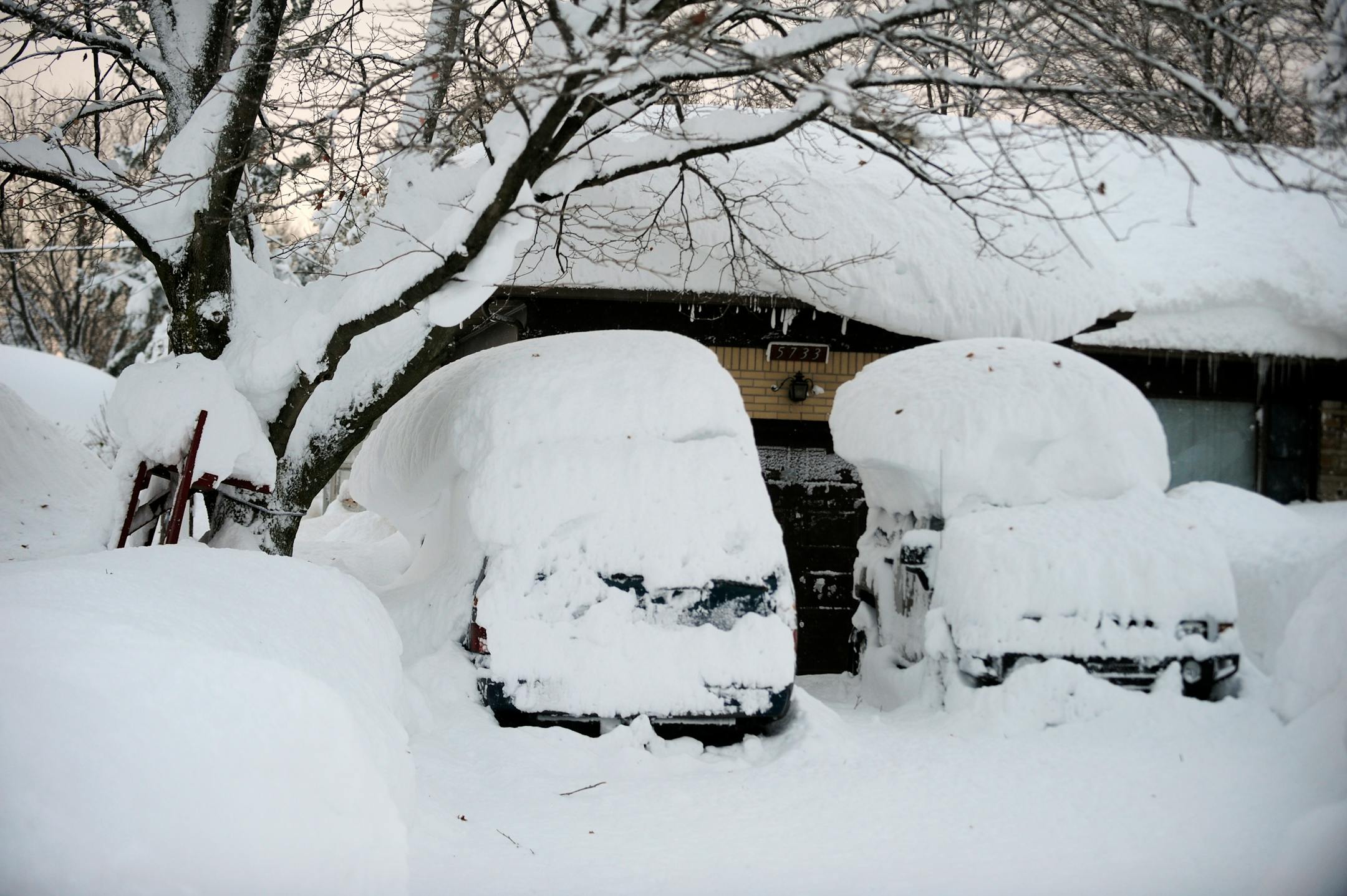 Cars with snow atop the roofs sit idle at this home on Broadway in Lancaster, N.Y. Wednesday, Nov. 19, 2014. A ferocious storm dumped massive piles of snow on parts of upstate New York, trapping residents in their homes and stranding motorists on roadways, as temperatures in all 50 states fell to freezing or below. (AP Photo/Gary Wiepert)