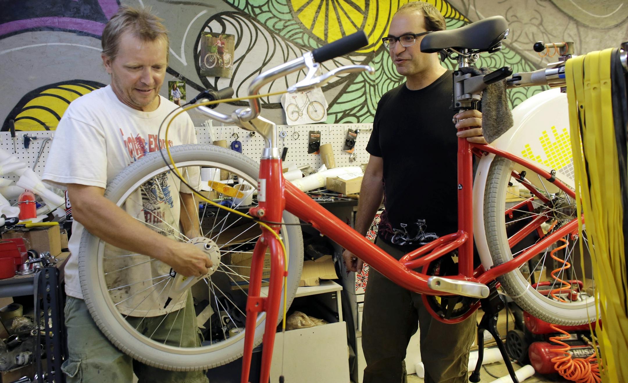 In this Tuesday, Aug. 4, 2015 photo, Avery Pack, president of Republic Bike, right, talks with employee Tim Hignett, left, as he assembles a fleet bicycle manufactured at Republic Bike, in Dania Beach, Fla. Companies, organizations and people are starting to forsake the familiar &#xec;.com&#xee; and &#xec;.org&#xee; Internet address suffixes, using instead hundreds of new ones like ".legal," ".movie," ".bike" and ".nyc" that have been coming on the market since early 2014. Using republic.bike is
