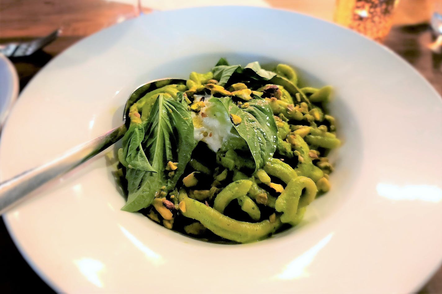 Green pasta with basil leaves and pistachios in a white bowl