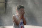 A child reacts to a mist machine as he cools off from the summer heat in Beijing, Saturday, June 15, 2024.