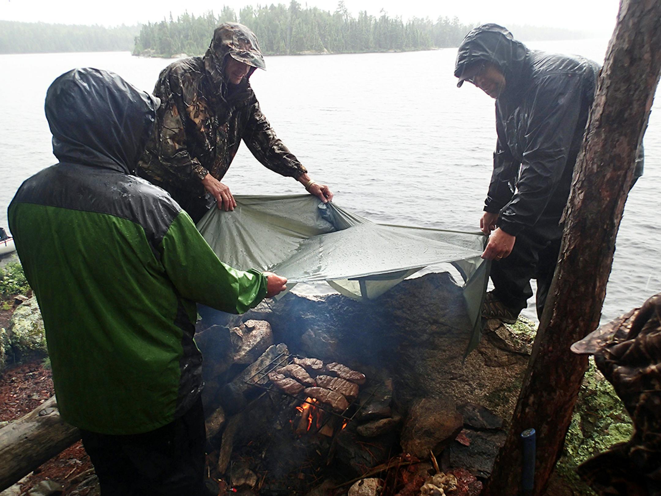 Campers hold a plastic poncho over a campfire as they try to finish cooking steaks during a rainstorm. Greg Swenson, right, later fell from his perch on the rock, but wasn't seriously hurt.