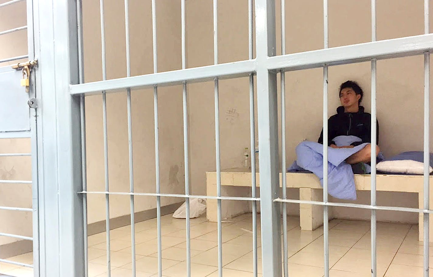 In his image provided by Initium Media Technology, Hong Kong journalist Hok Chun Anthony Kwan sits in a cell Monday, Aug. 24, 2015, after he was detained Sunday at Suvarnabhumi Airport in Bangkok, Thailand, for carrying body armor and a helmet onto a flight bound for Hong Kong.