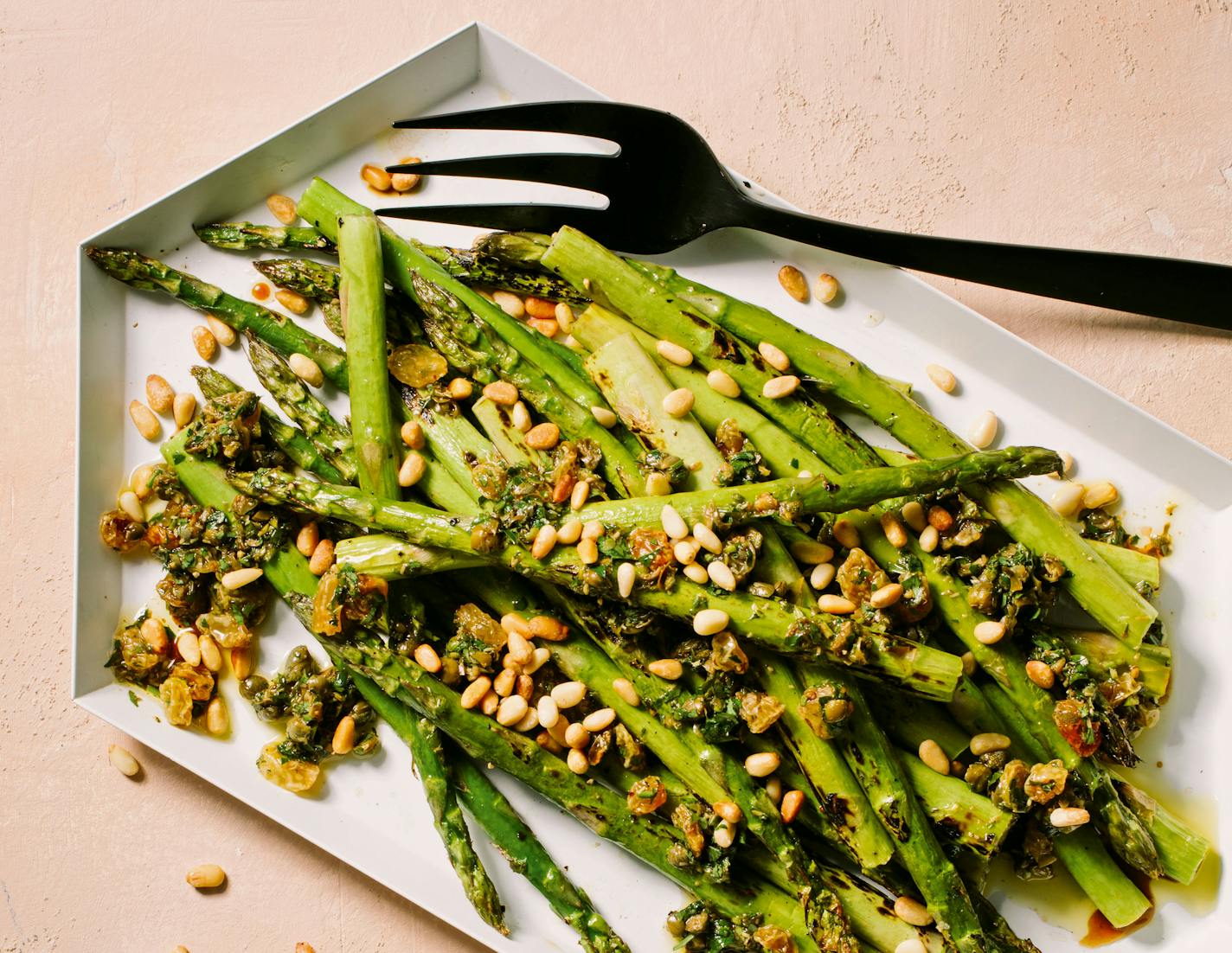 A platter of charred asparagus with caper-raisin relish and topped with pine nuts.