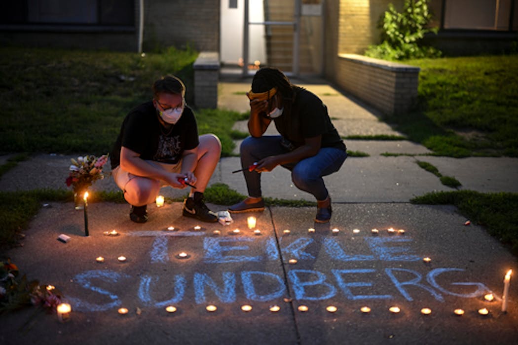Marcia Howard, activist and George Floyd Square caretaker, right, lighted candles during a vigil for 20-year old Andrew Tekle Sundberg Thursday, July 14, 2022 outside the apartment building where he was killed by Minneapolis police.