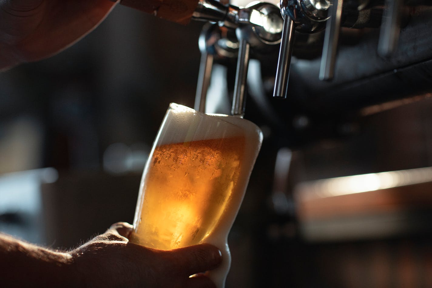 Fresh beer filling the glass directly from the tap. With extra foam spilling over glass.