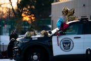 The sun sets behind a police car covered in flowers and balloons outside of Burnsville City Hall in honor of the two police officers and a paramedic k