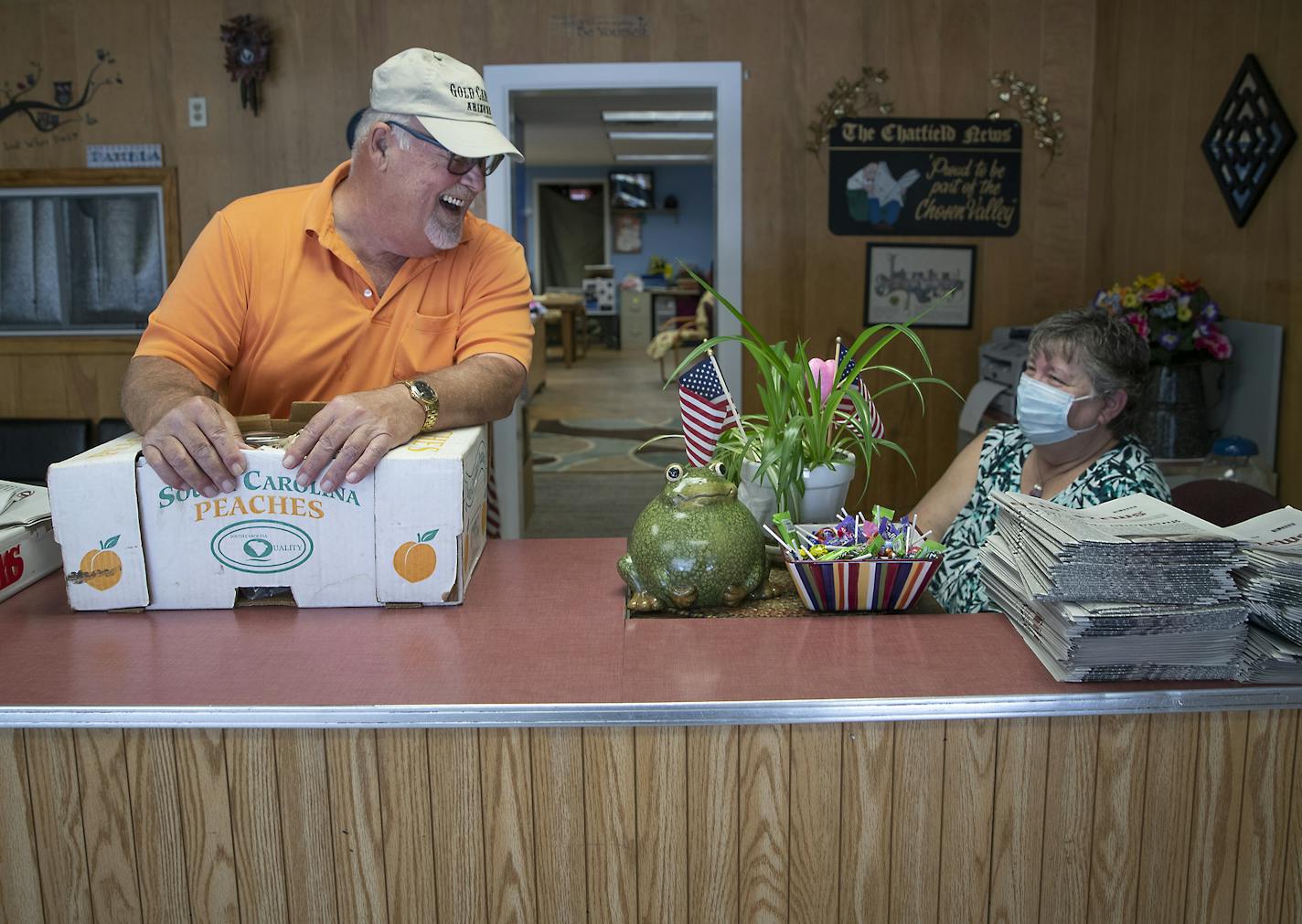 Lonny Berge, who once worked at the Chatfield News, picked up a box of pickles and caught up with Pam Bluhm in the newspaper office, Monday, August 3, 2020 in Chatfield, MN. Bluhm worked at the Chatfield News for nearly half of its 96-year history. When the newspaper serving Olmsted and Fillmore counties closed earlier this year, Bluhm was out of a job. With encouragement from friends and neighbors, she resurrected the paper with her stimulus check and now is singlehandedly keeping it alive. ] E