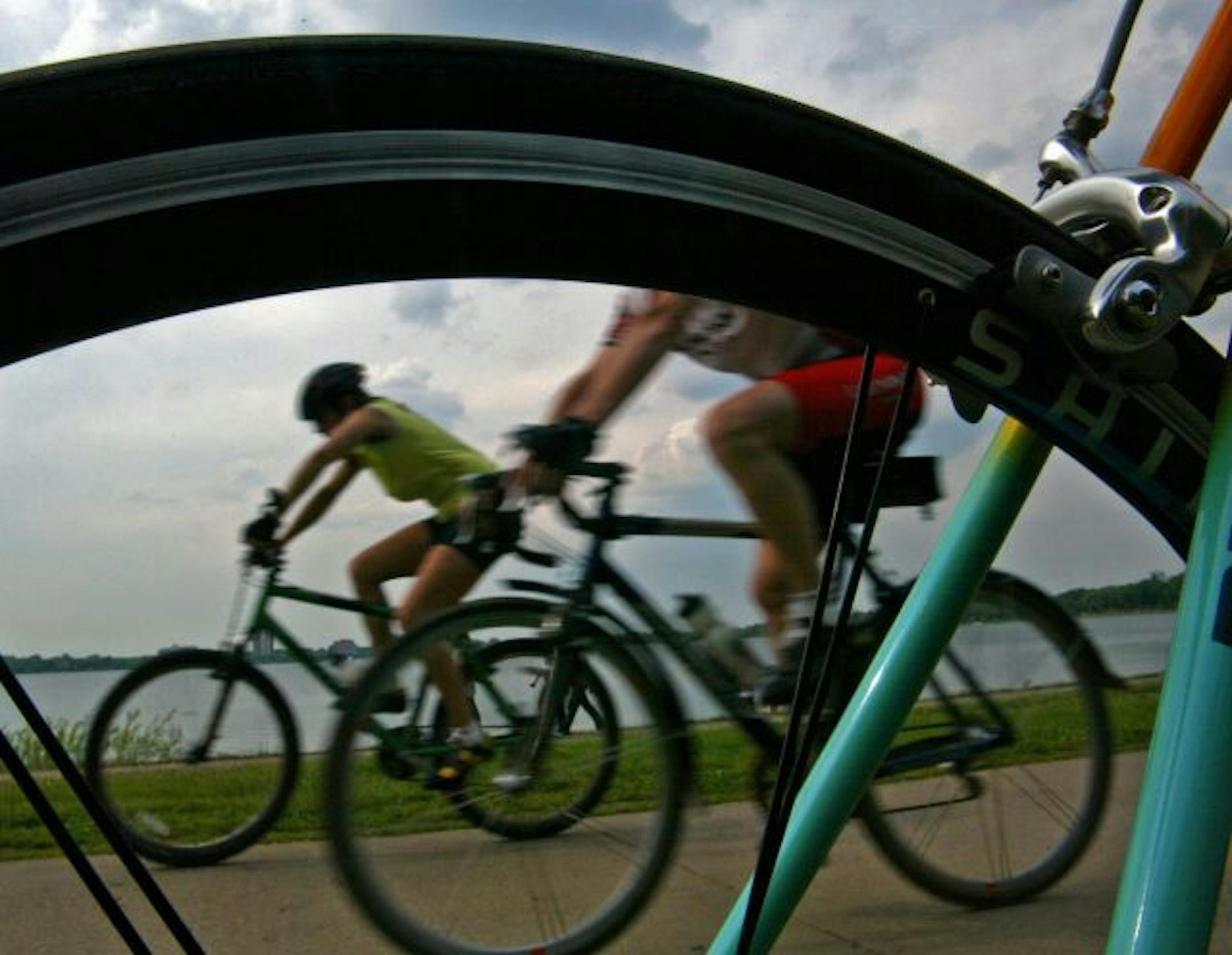 star tribune staff tom sweeney Minneapolis, Mn 6/02/2005 a pair of cyclists, one riding a mountain bike, the other a 'commuter' framed through the wheel of a road racing bike as they ride the path at lake calhoun