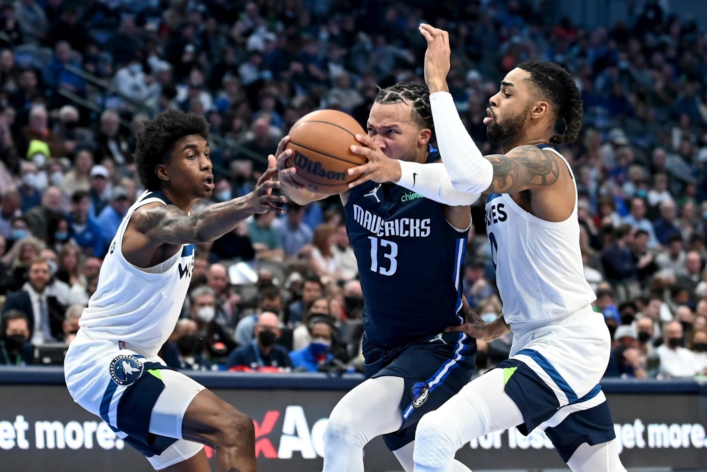 Minnesota Timberwolves forward Jaden McDaniels, left, and D'Angelo Russell, right, defend against a drive to the basket by Dallas Mavericks' Jalen Brunson, center, in the first half of an NBA basketball game in Dallas, Tuesday, Dec. 21, 2021. (AP Photo/Matt Strasen)